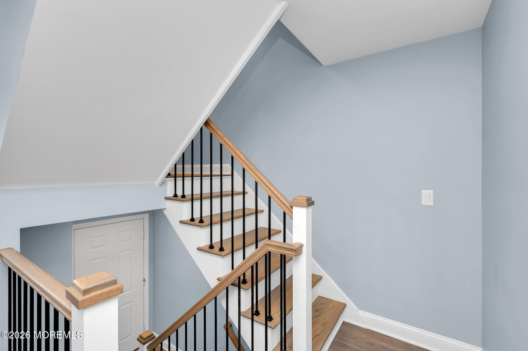 Staircase with wood treads and handrails, black metal balusters, and pale blue walls.