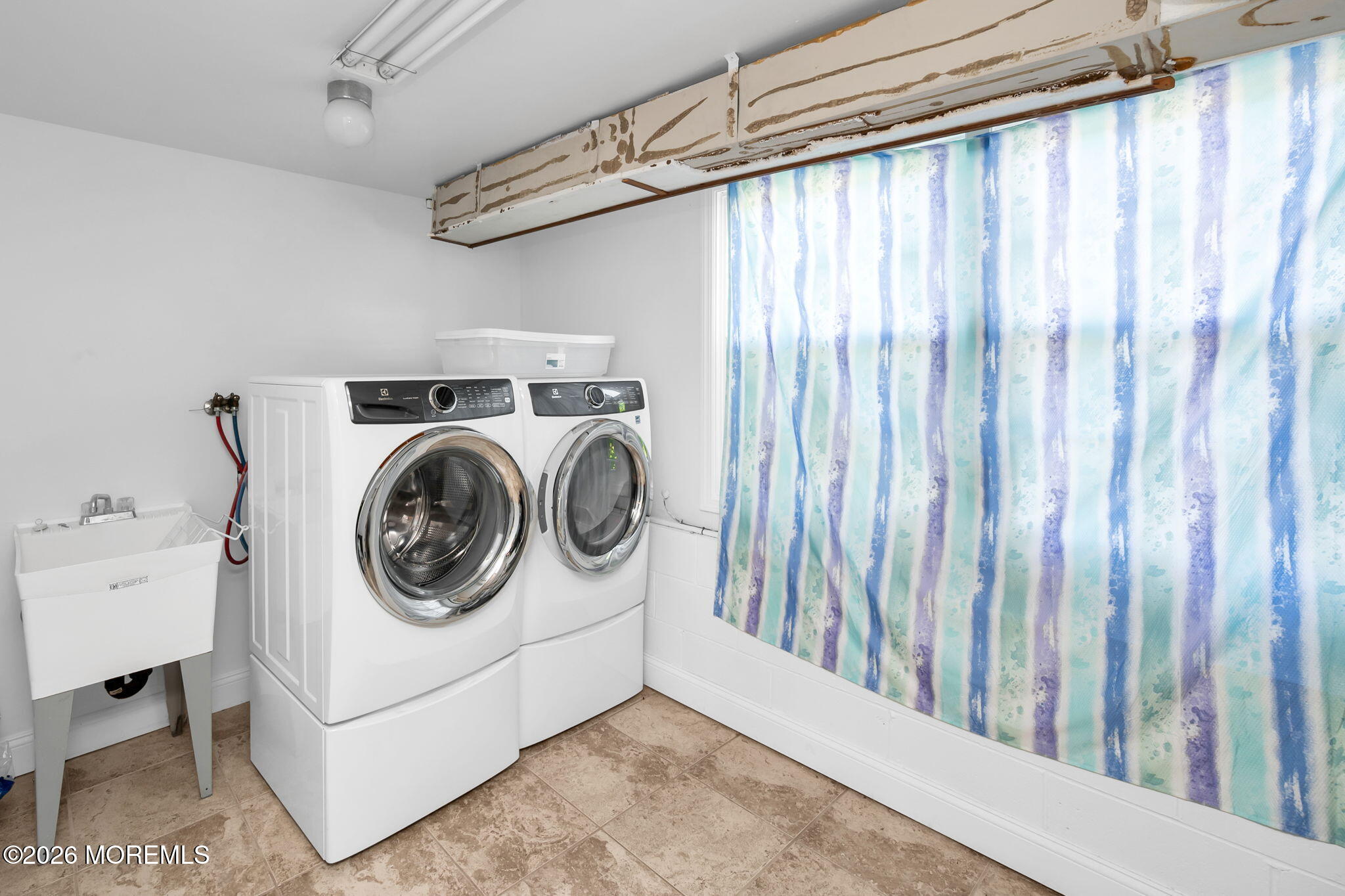 Laundry room with front-loading washer and dryer, utility sink, and blue-green striped curtain.