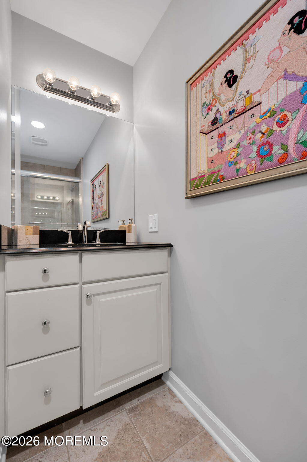 Bathroom vanity with black countertop, large mirror, and colorful framed artwork.