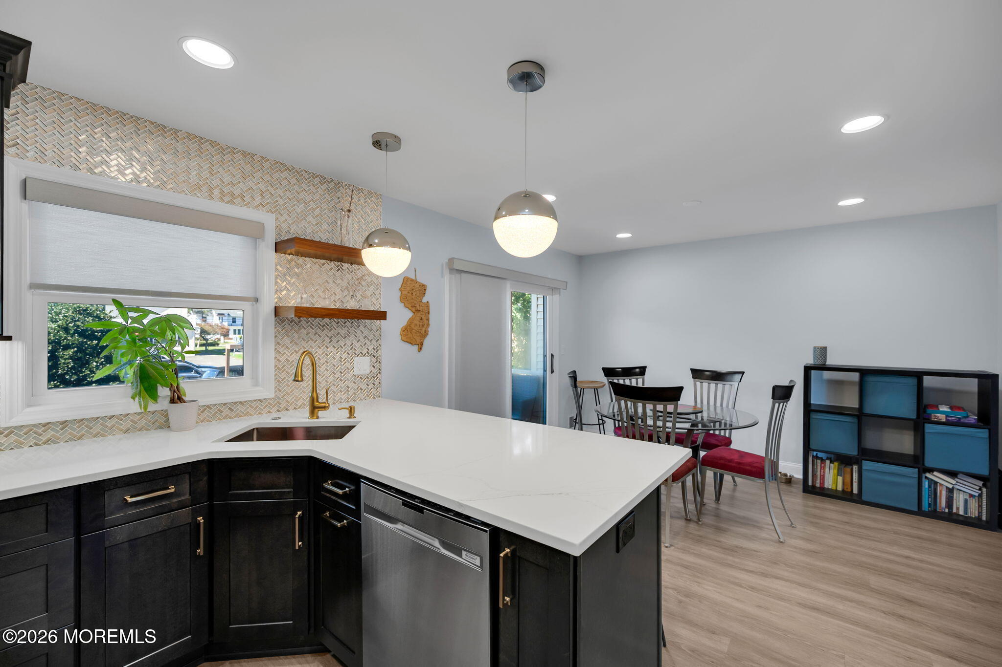 Kitchen with a large white island, dark cabinets, patterned backsplash, and adjoining dining area.