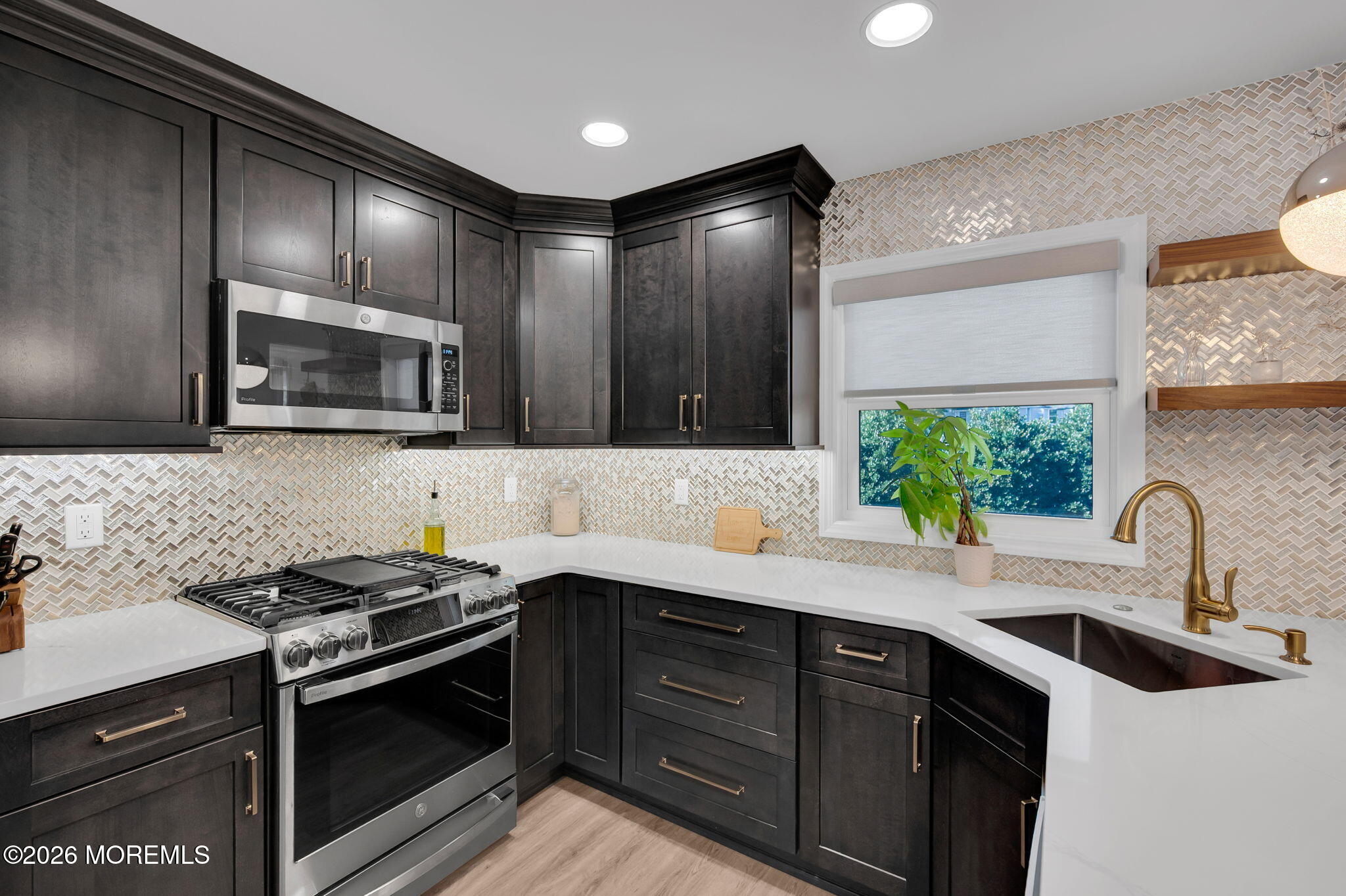 Renovated kitchen with dark cabinetry, patterned tile backsplash, stainless steel range, and brass sink fixtures.