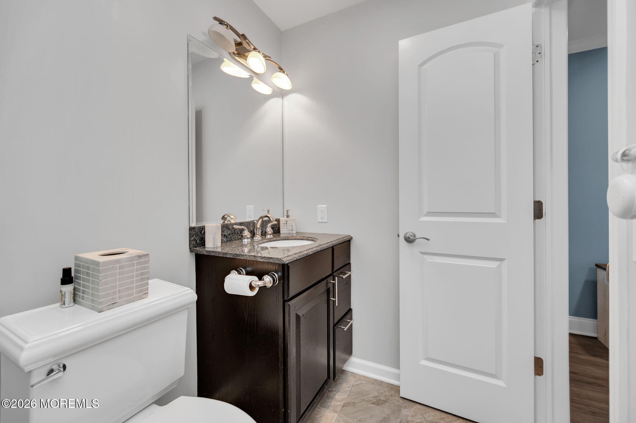 Bathroom with dark wood vanity, granite countertop, large mirror, and open door to a blue-walled room.