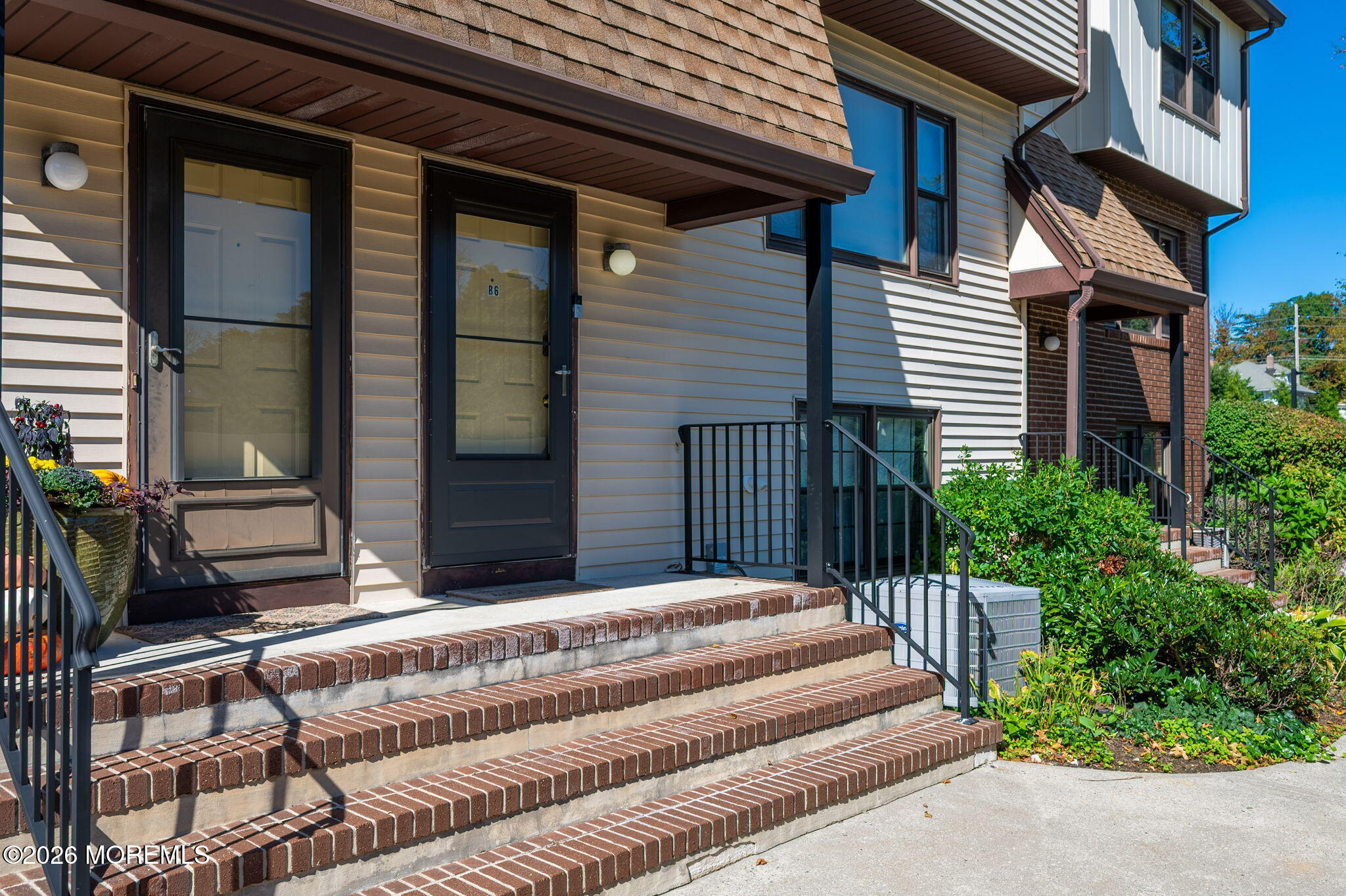Unit B6 entrance with a dark door, brick steps, black railings, and landscaped shrubs.