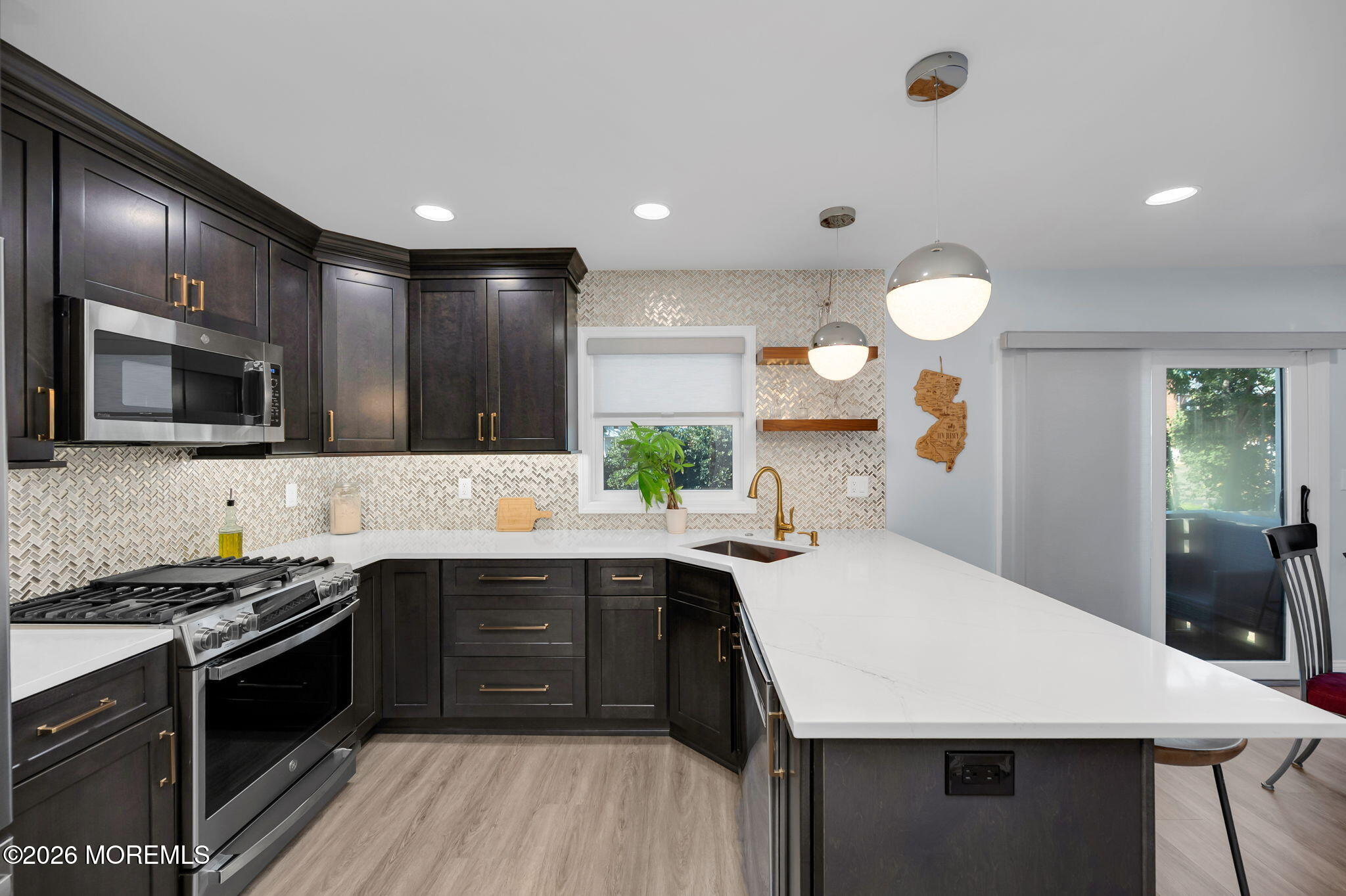 Renovated kitchen with dark cabinets, patterned tile backsplash, stainless range, and a large white island.