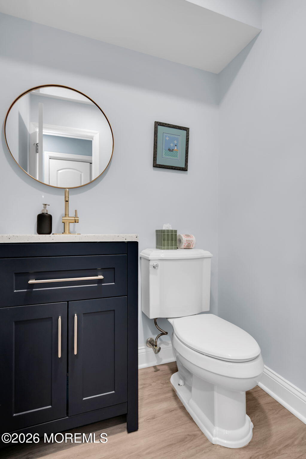 Bathroom with a navy vanity, round mirror, gold faucet, and white toilet.