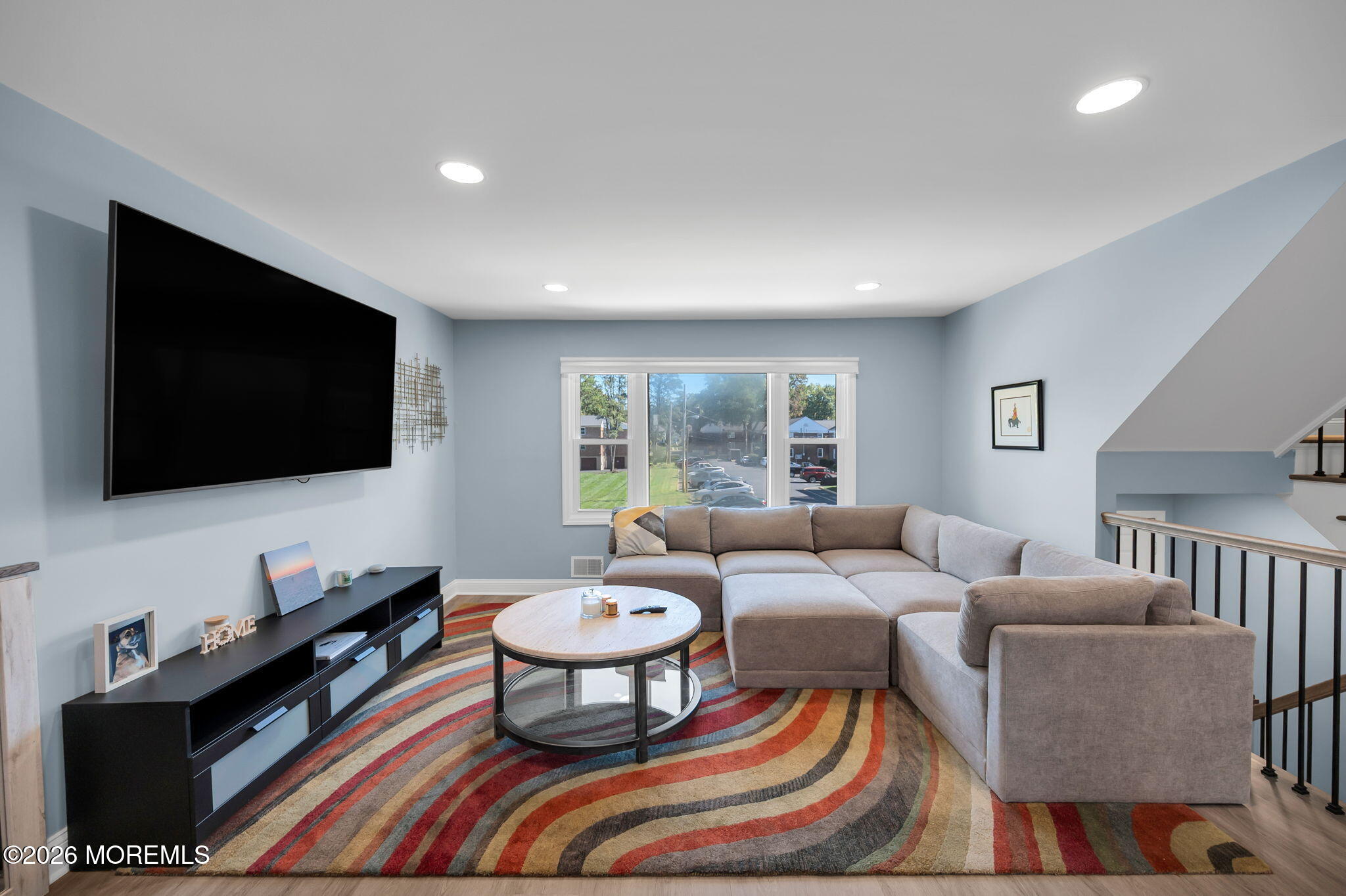 Living room with a gray sectional, wall-mounted TV, and colorful striped rug.