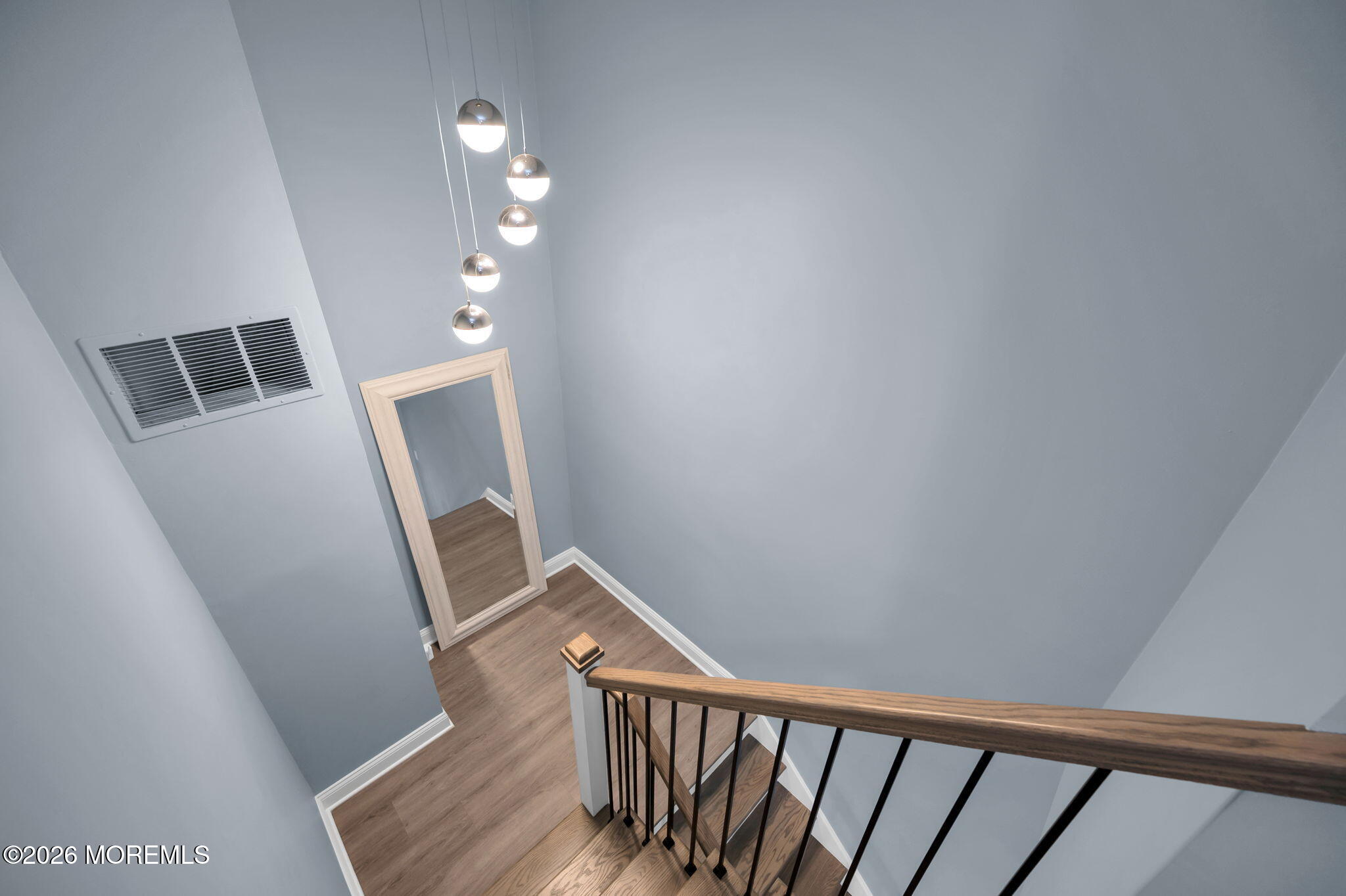 Staircase with wood flooring, black metal balusters, and pendant lights above a mirrored landing.