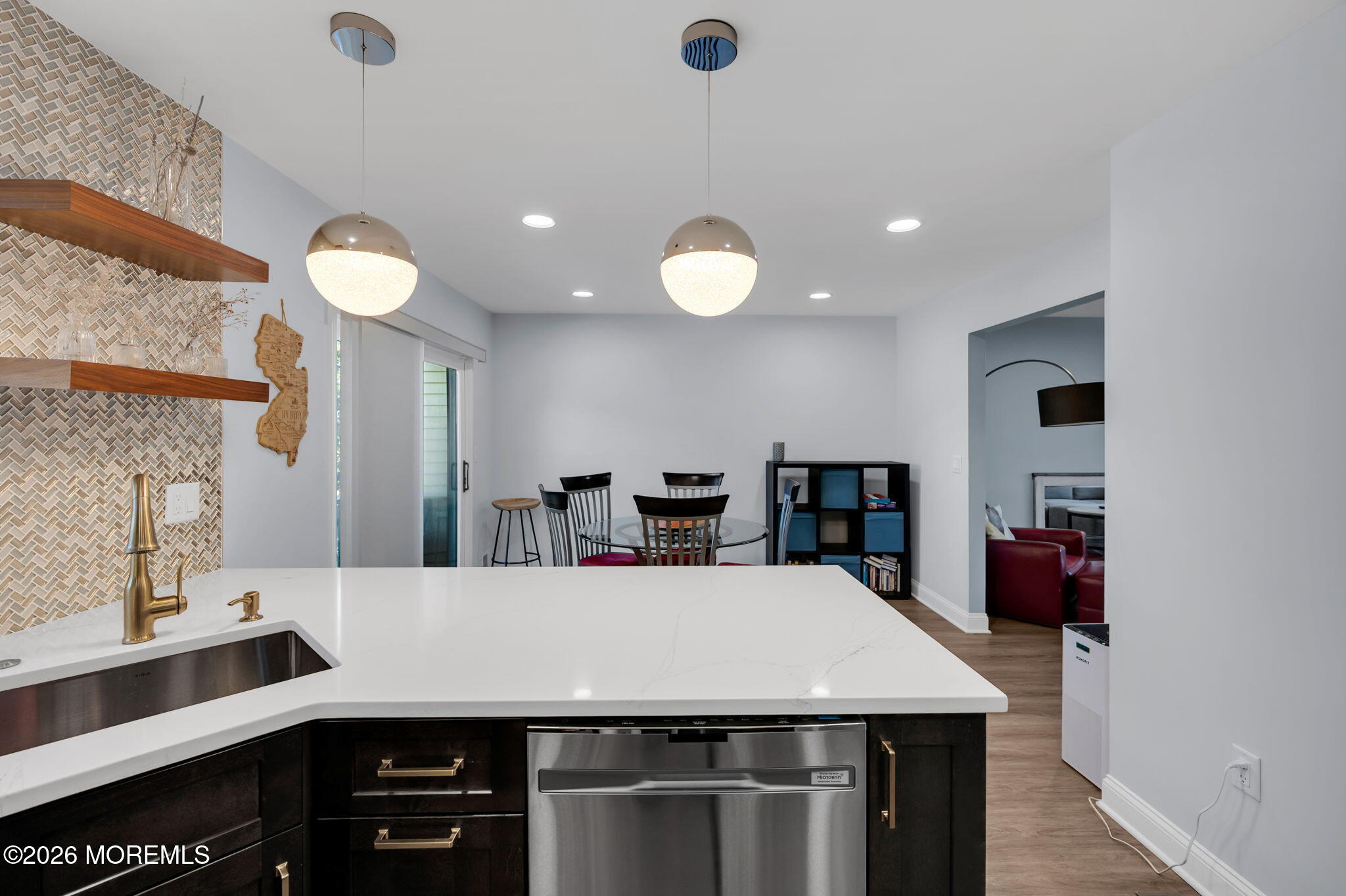 Modern kitchen with a large quartz island, brass faucet, patterned backsplash, and dining area.