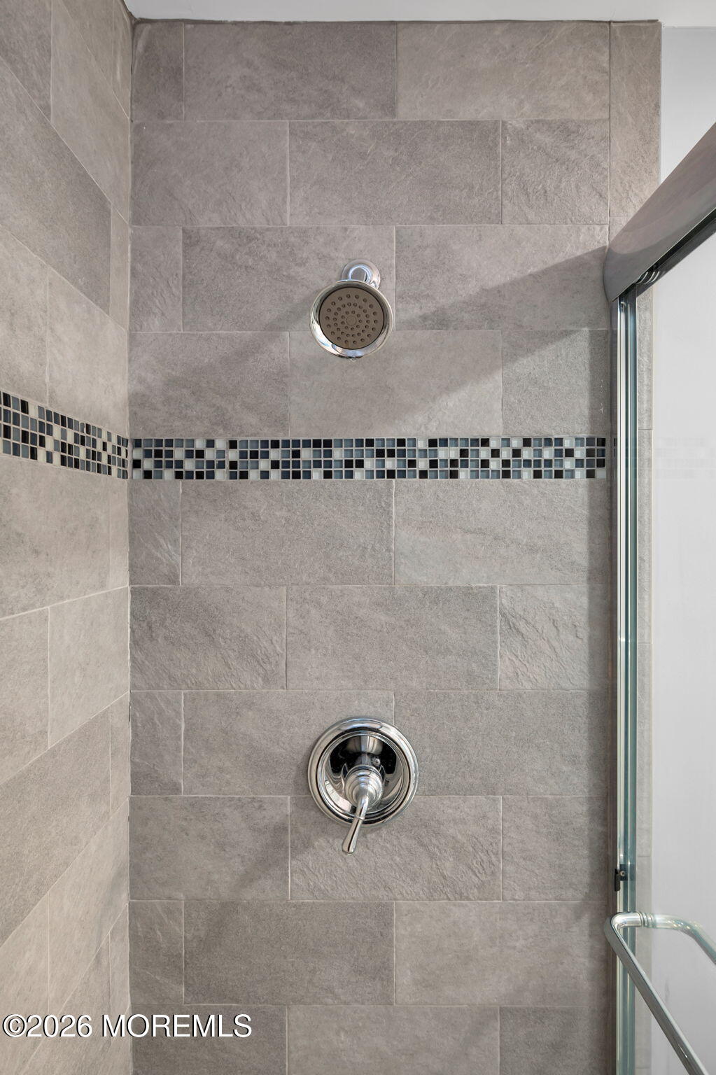 Tiled shower with a mosaic accent band, chrome fixtures, and a glass enclosure.