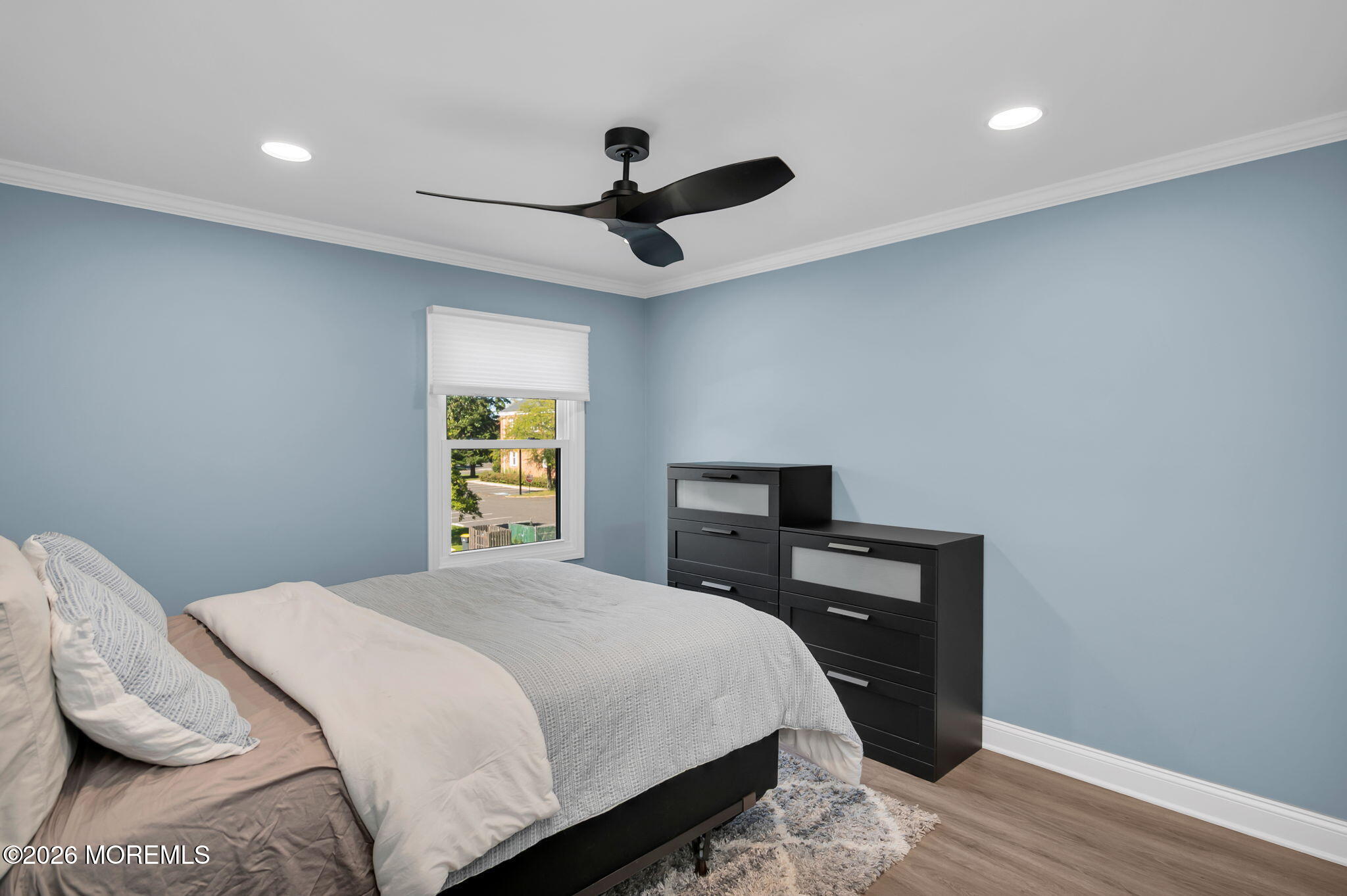 Bedroom with a neatly made bed, blue walls, black dresser, and ceiling fan.