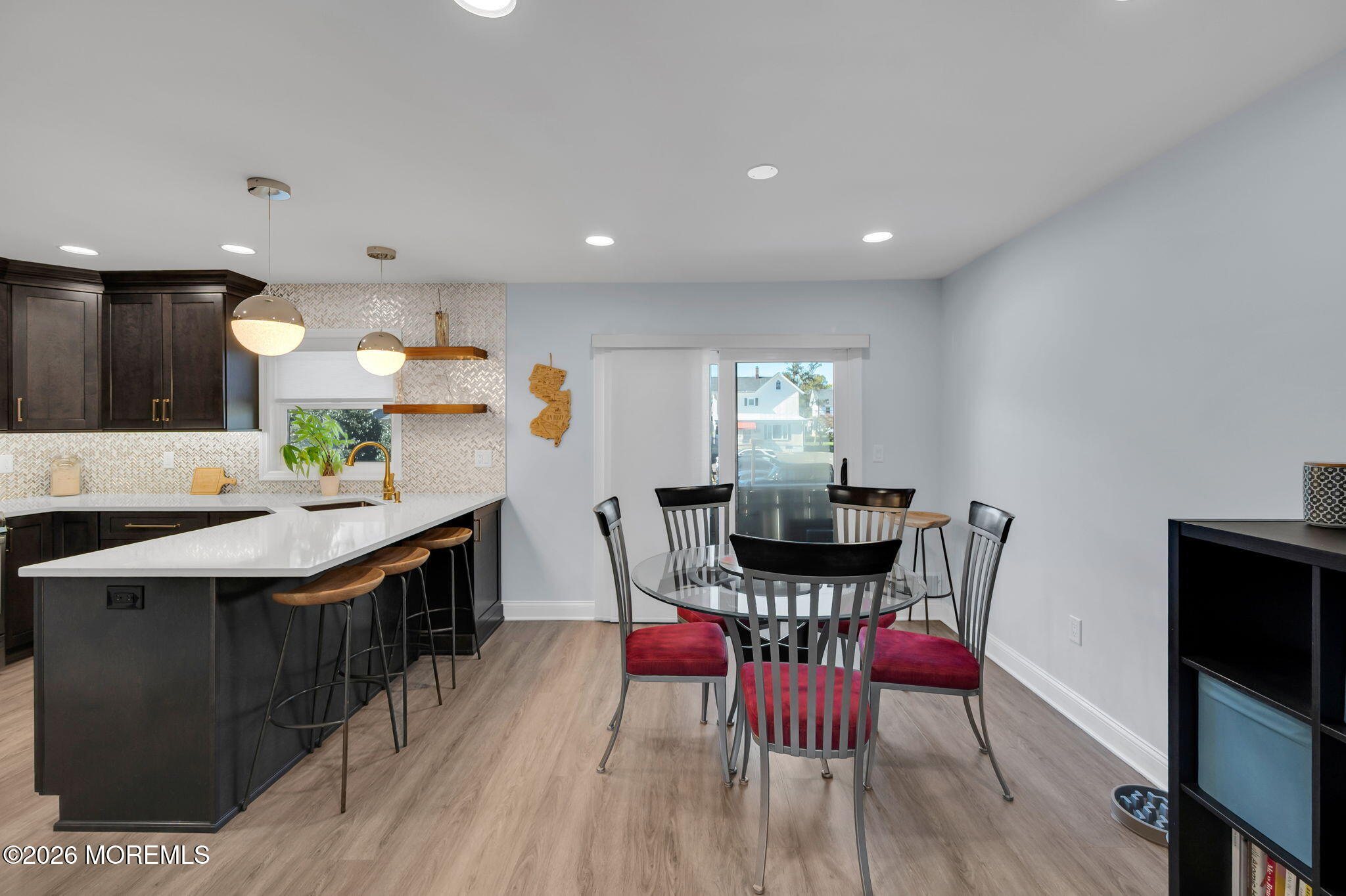 Kitchen and dining area with dark cabinets, white peninsula, patterned backsplash, and red-cushioned dining chairs.