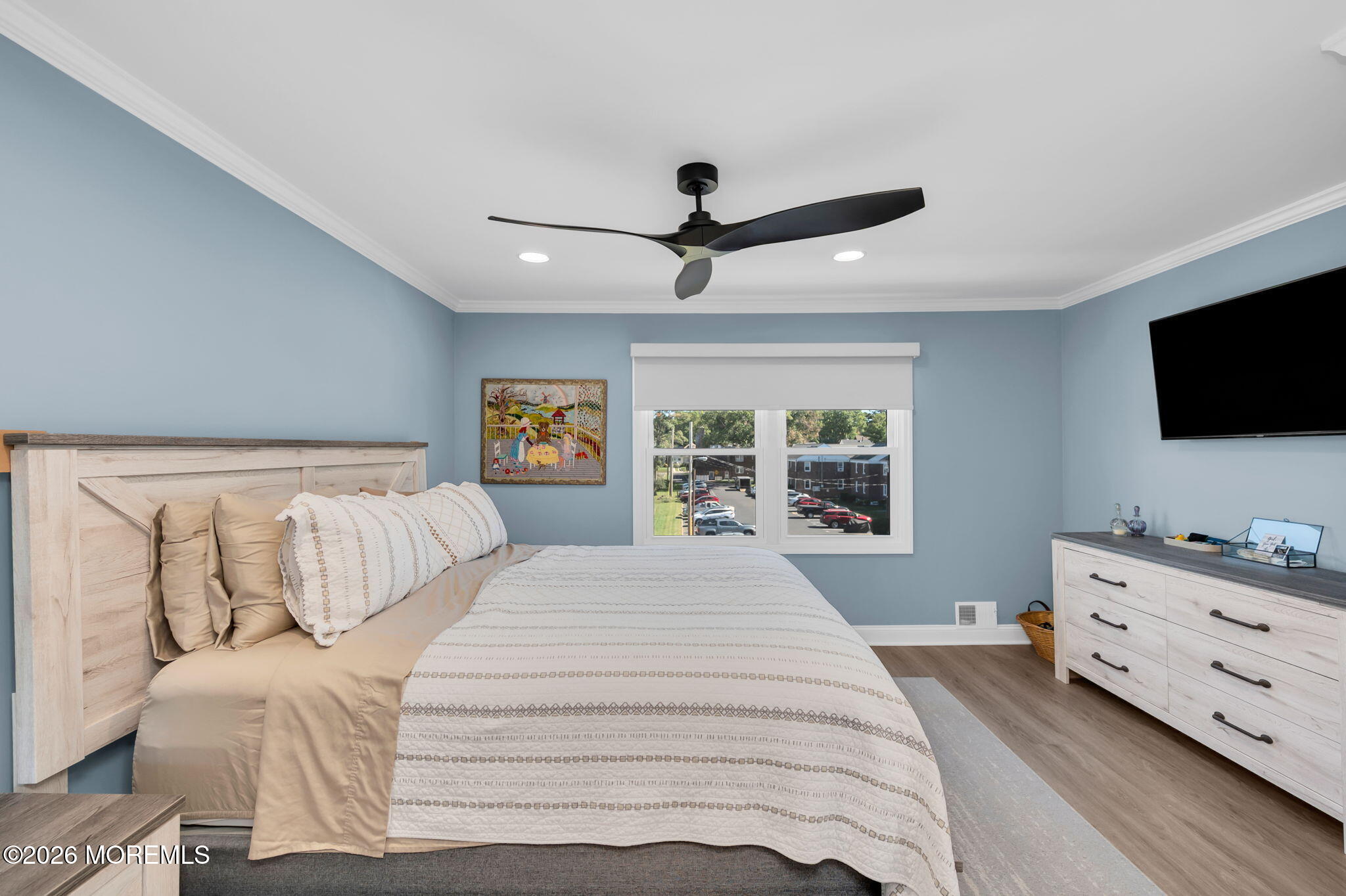 Staged bedroom with blue walls, a patterned white bedspread, and a light wood dresser.