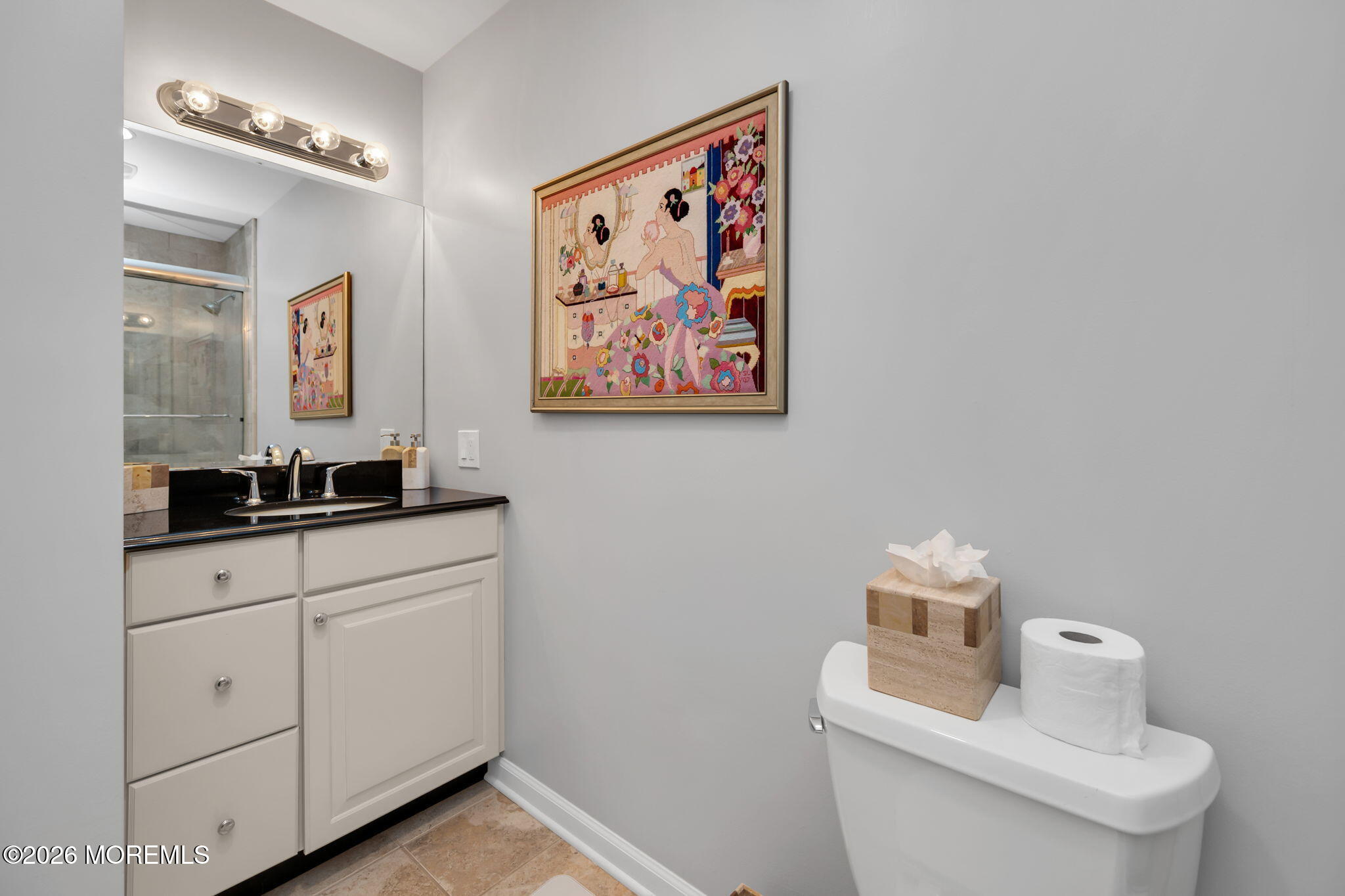 Bathroom with a black-countertop vanity, tiled shower, and colorful framed artwork above the toilet.