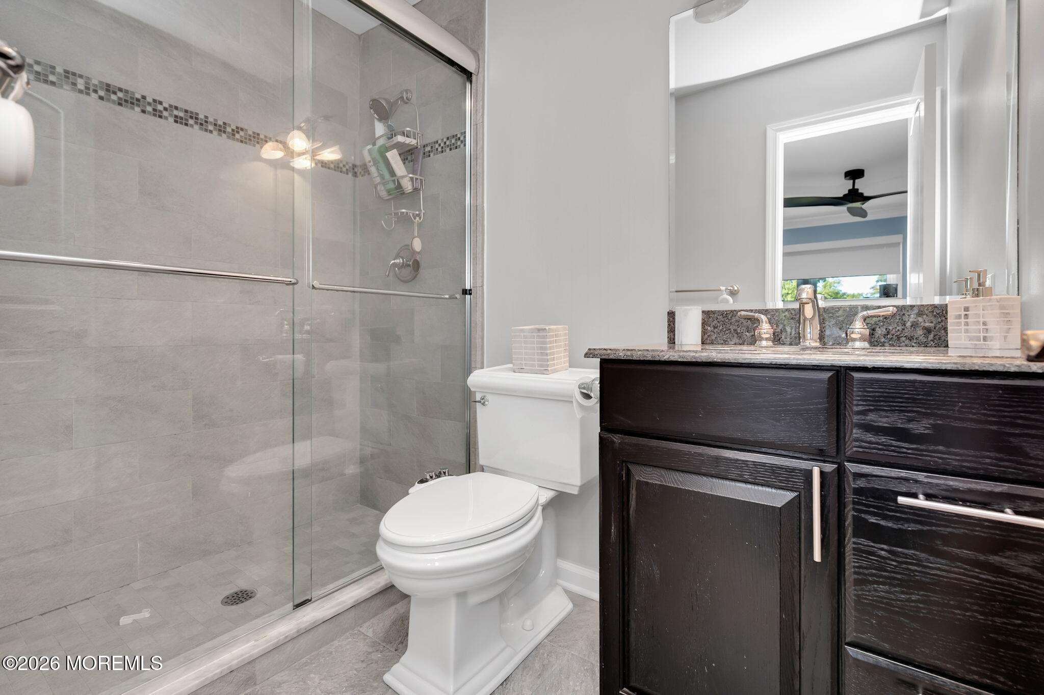 Bathroom with a glass-enclosed tiled shower and dark wood vanity with stone countertop.