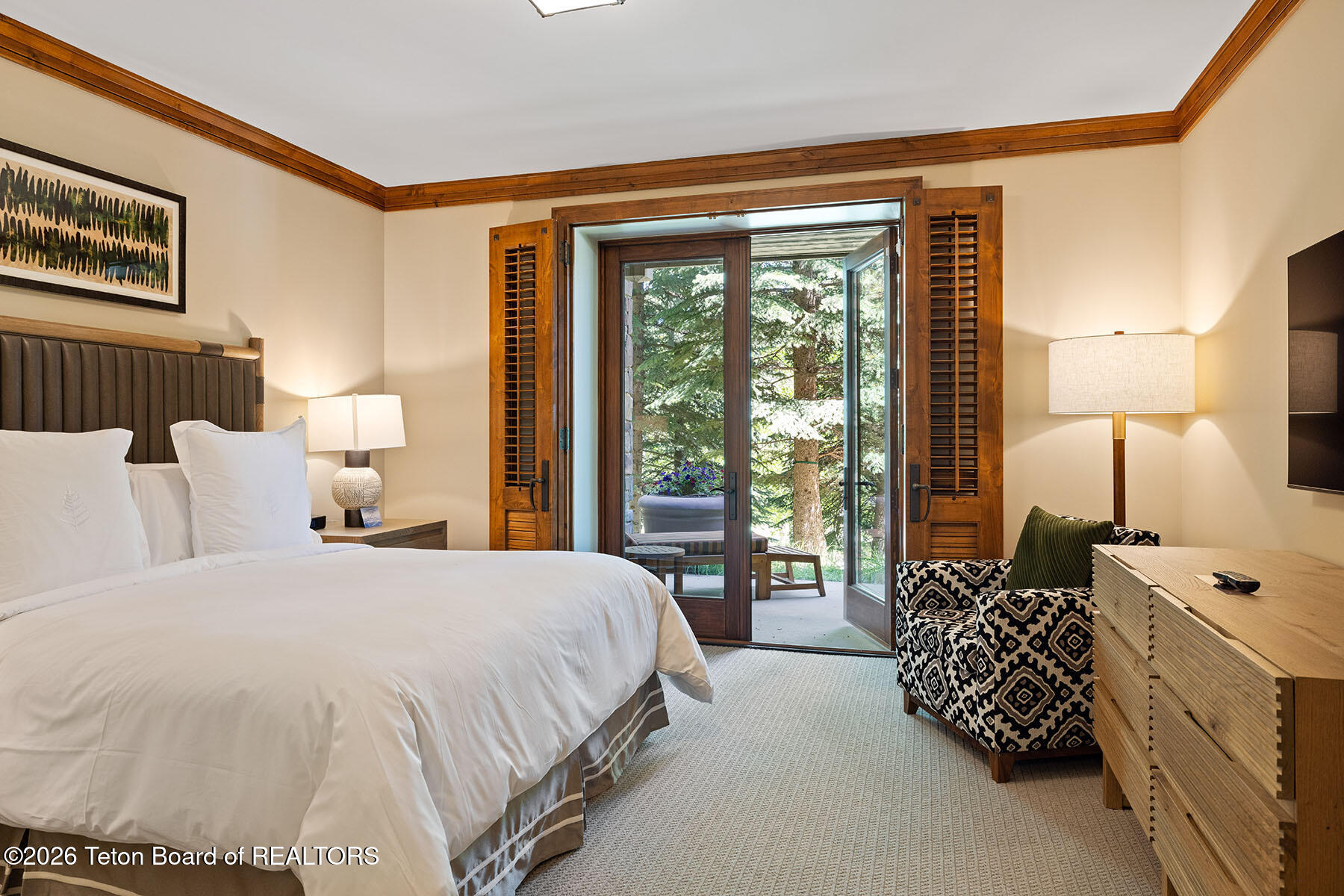 Bedroom with a white bed and open patio doors overlooking trees.