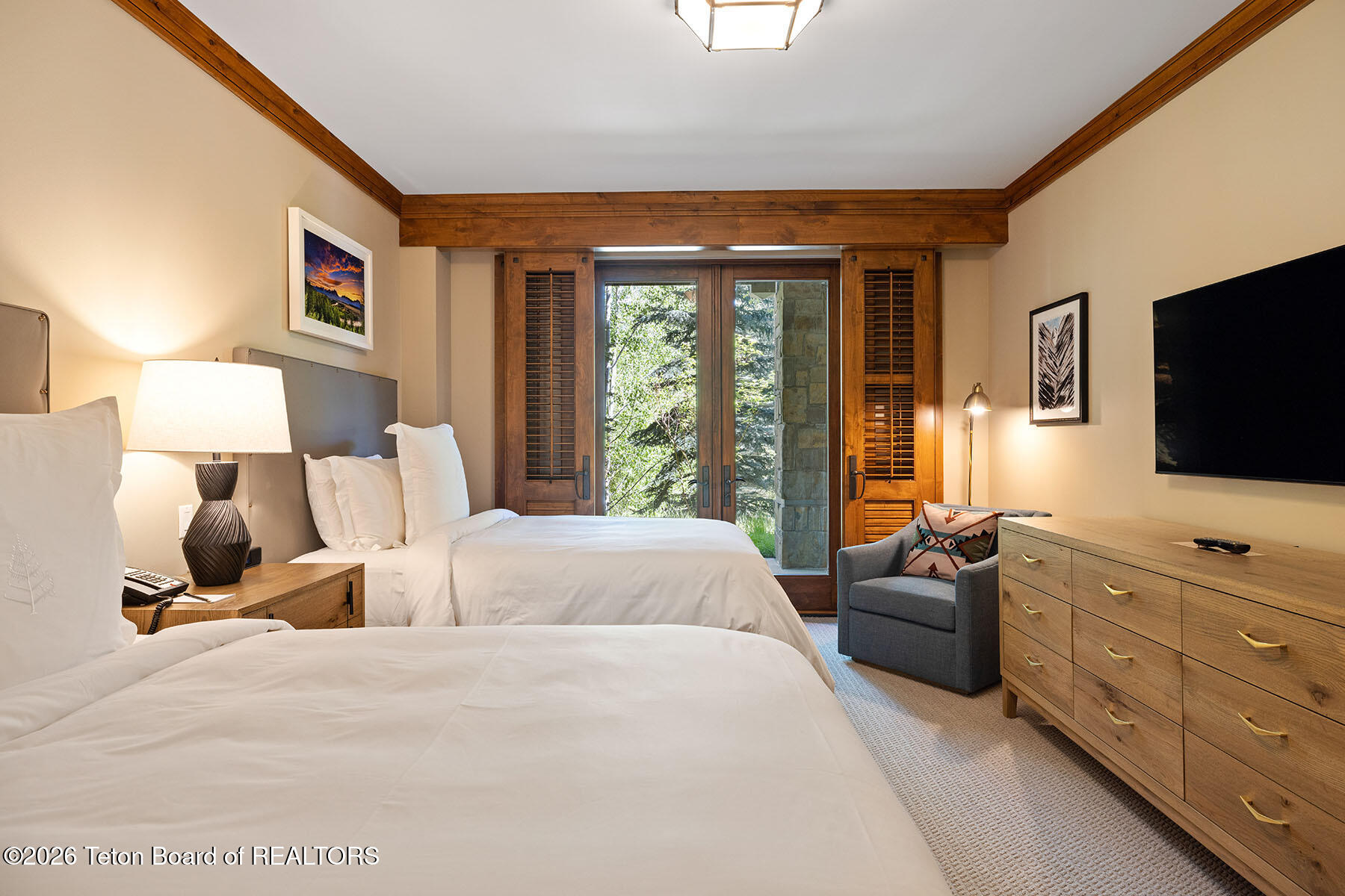 Furnished bedroom with two beds, wood-trimmed doors, and a gray sitting area.