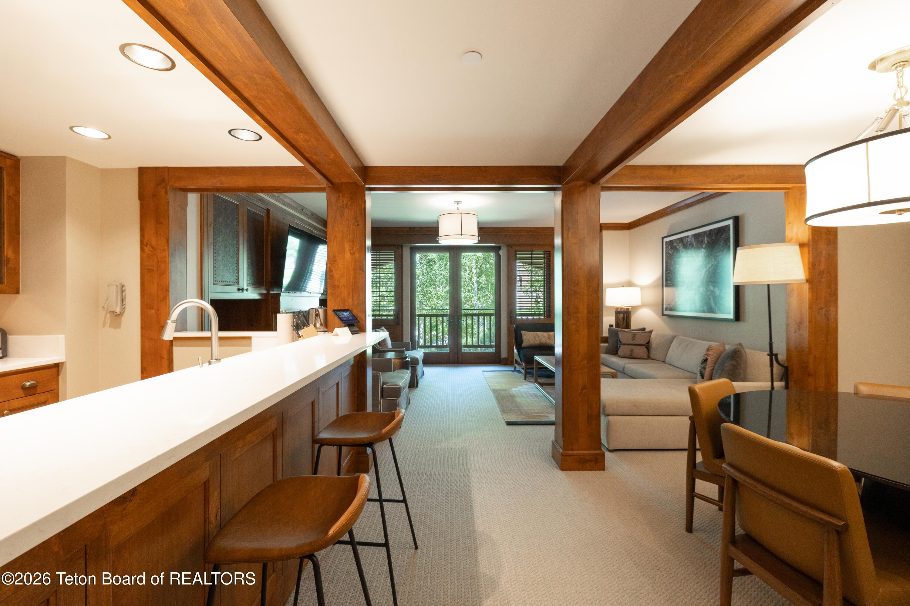 Open-plan kitchen and living area with a long white breakfast bar and exposed wood beams.