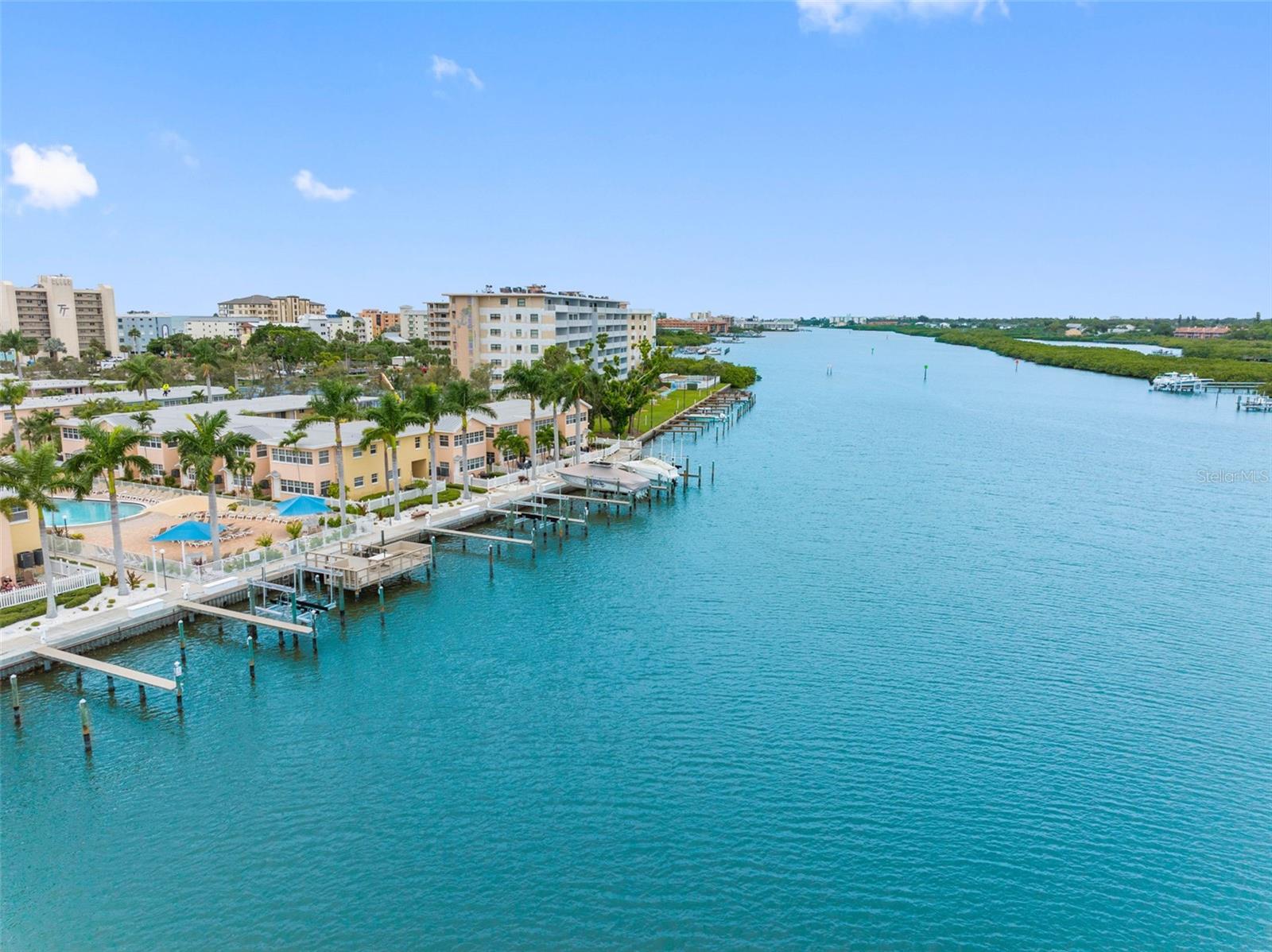 Aerial view of waterfront condominiums, docks, and a pool along a broad blue channel.