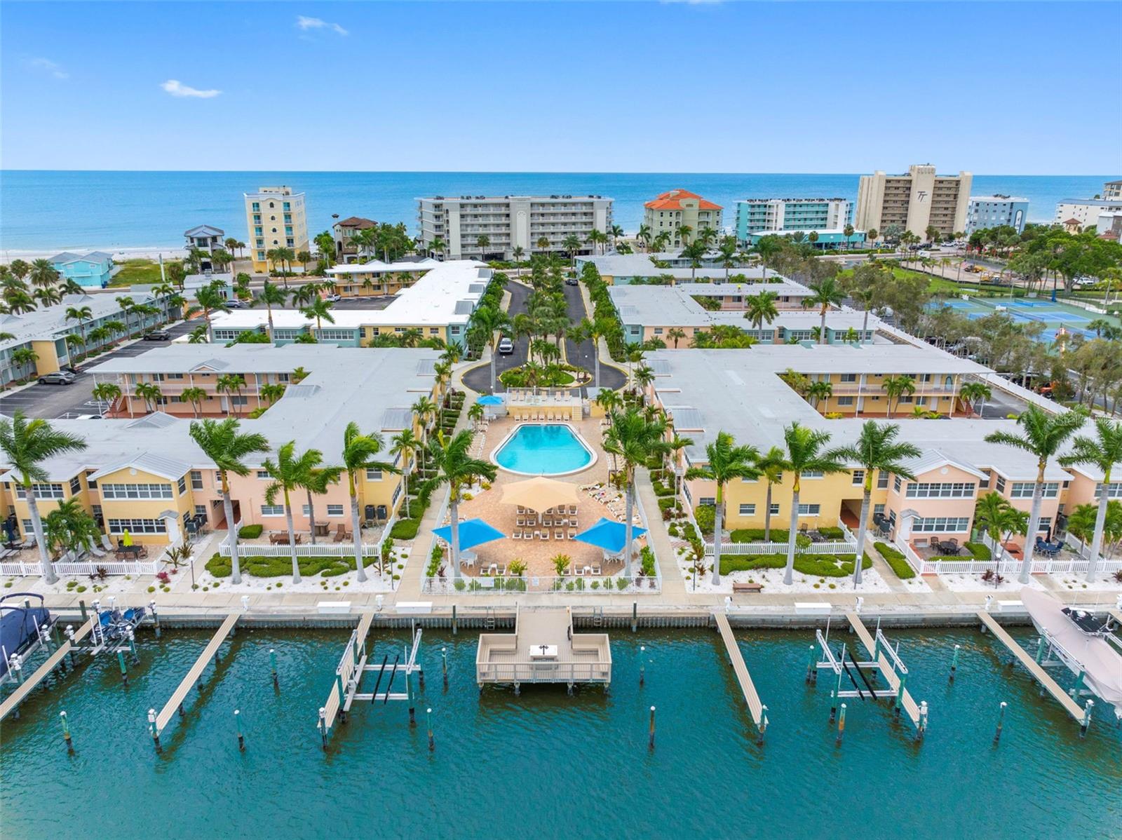 Aerial view of a waterfront condominium complex with a central pool, boat slips, and the Gulf beyond.