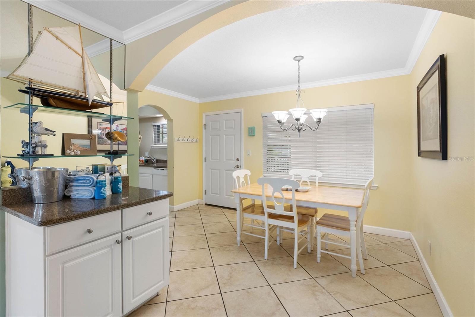 Dining area with a white table and chairs beside a kitchen counter and mirrored display shelves.