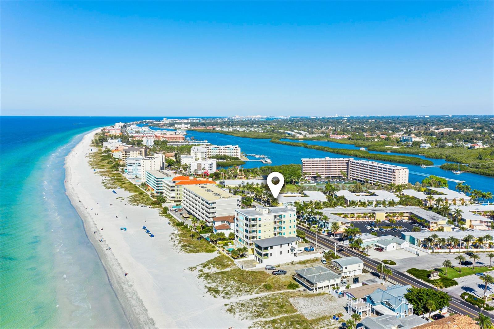 Aerial view of beachfront condos, white sand, turquoise Gulf water, and a nearby inlet.