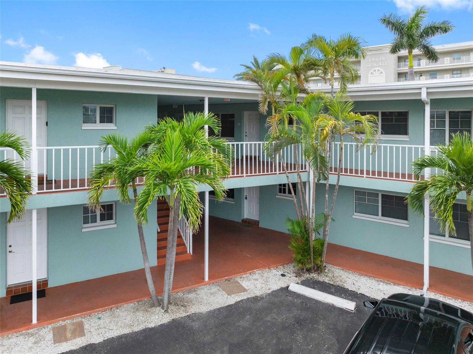 Two-story turquoise condominium courtyard with white railings, palm trees, and covered walkways.