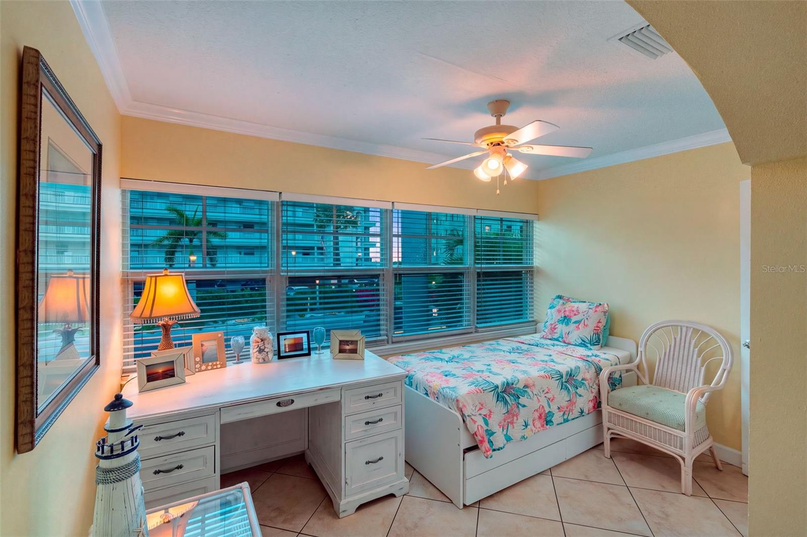 Bedroom with a floral-covered twin bed, white dresser, and wide windows with blinds.