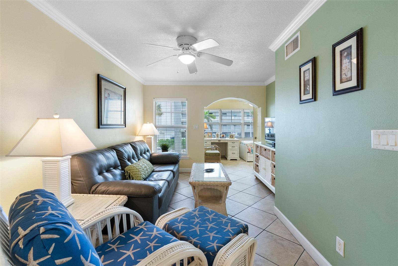 Furnished living room with a dark leather sofa, blue starfish-print chairs, and tiled floors.