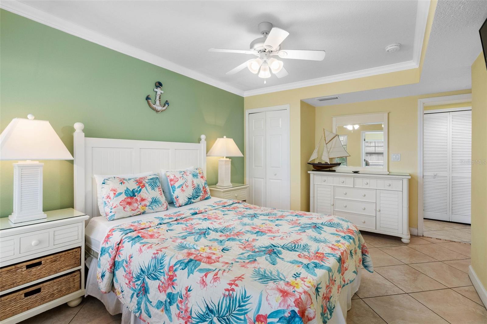 Bedroom with a floral bedspread, green accent wall, and white dresser topped with a sailboat model.