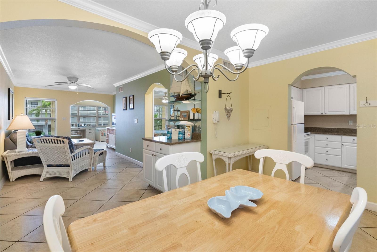 Open dining and living area with a wood table, white wicker seating, and an adjoining kitchen.