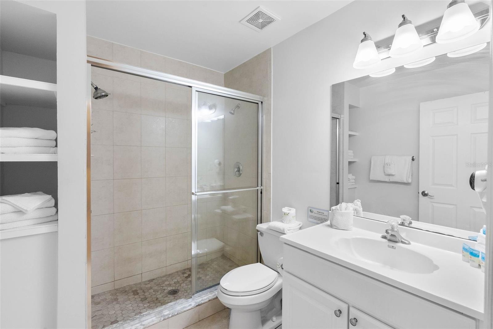 Bathroom with a glass-enclosed tiled shower, white vanity, and toilet.