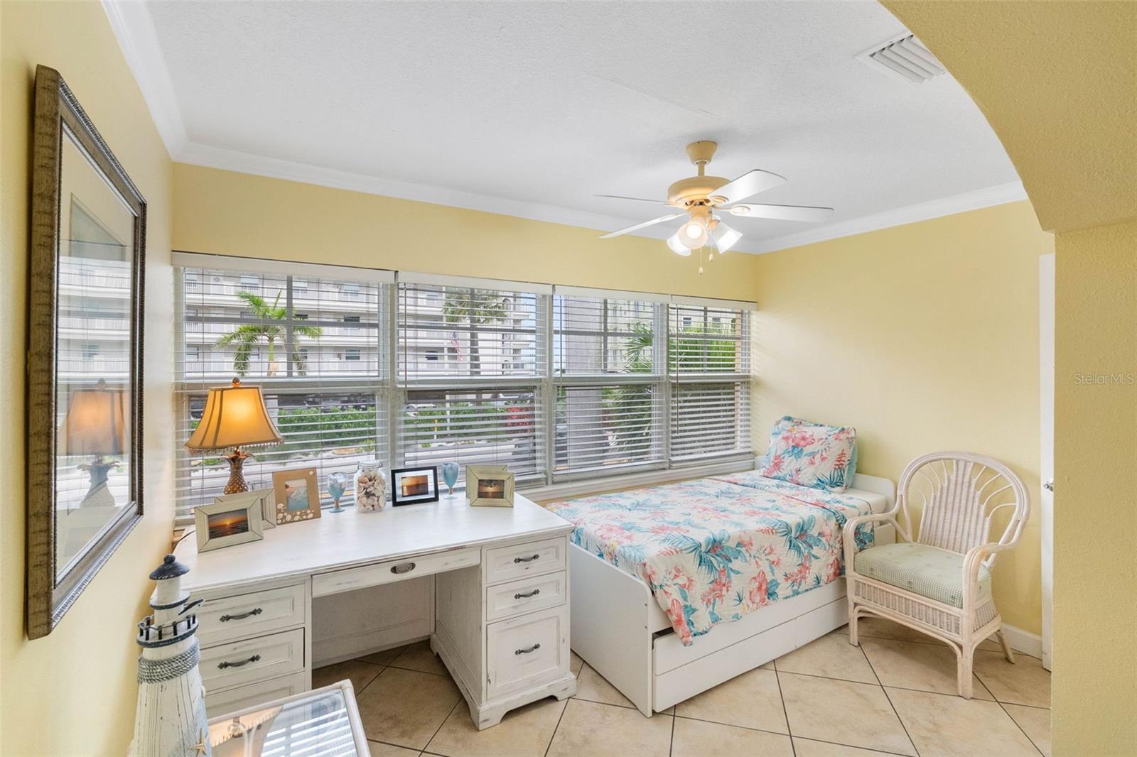 Bedroom with a floral daybed, white desk, and wide windows with blinds.