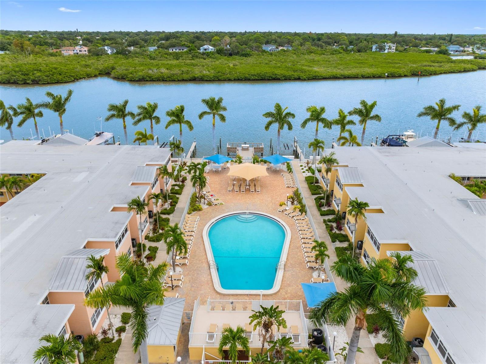 Aerial view of a waterfront condominium courtyard with a pool, palm trees, and boat docks.