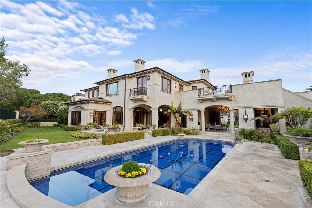 Mediterranean-style home with a blue pool, stone patio, and landscaped grounds.