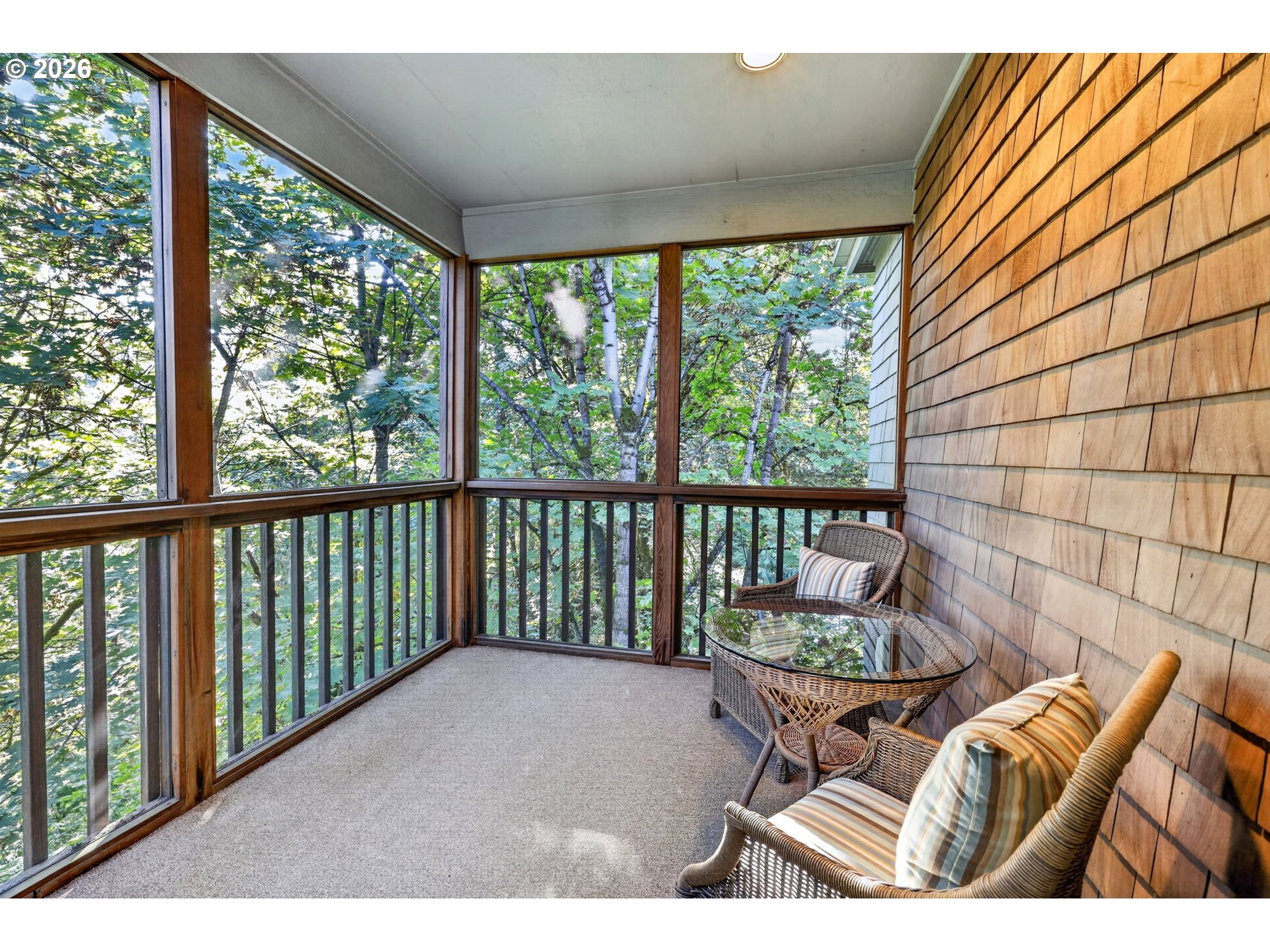 Screened-in porch with wicker seating and a leafy wooded view.