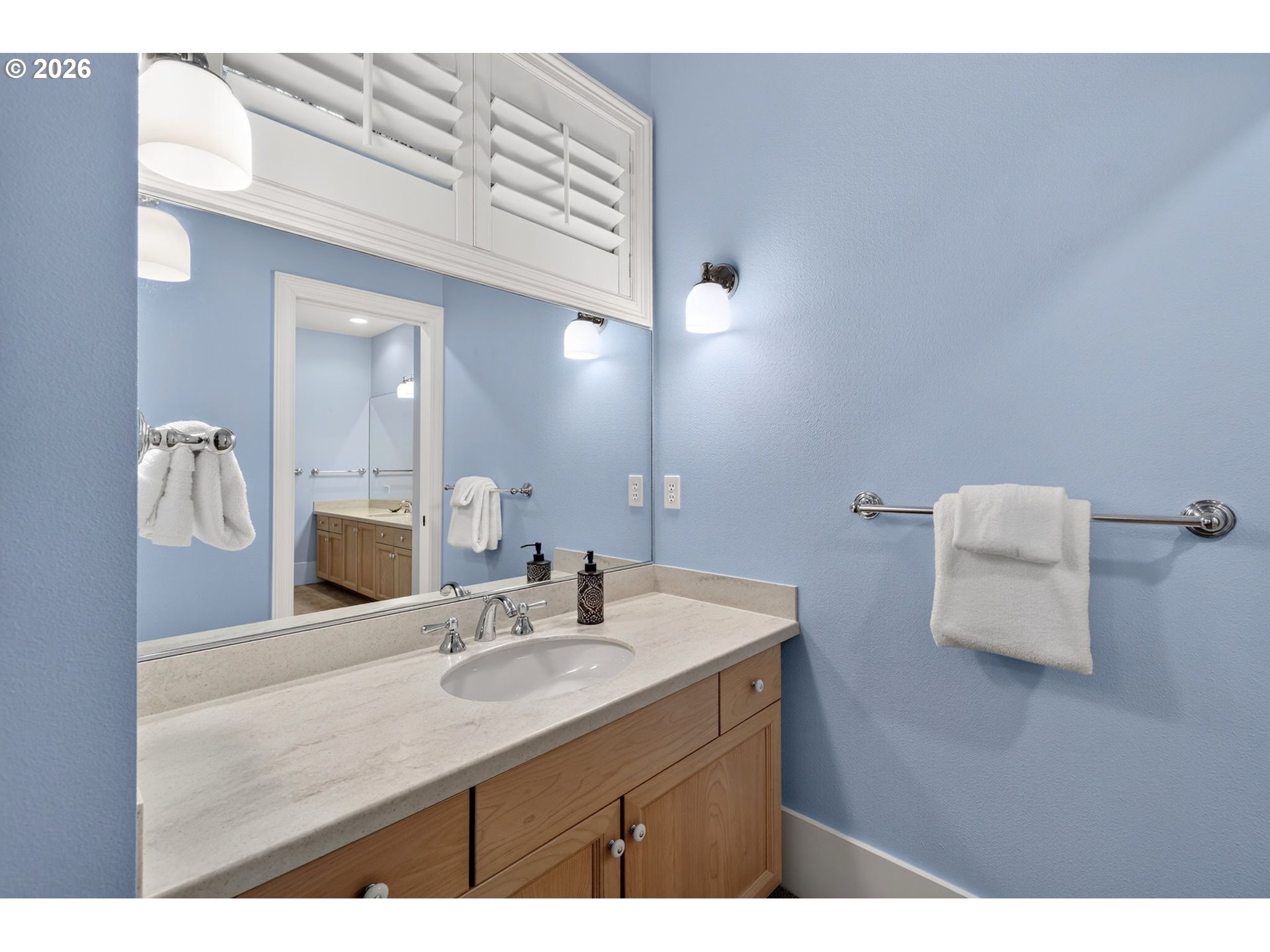 Bathroom vanity with a large mirror, pale blue walls, and white towels on chrome bars.