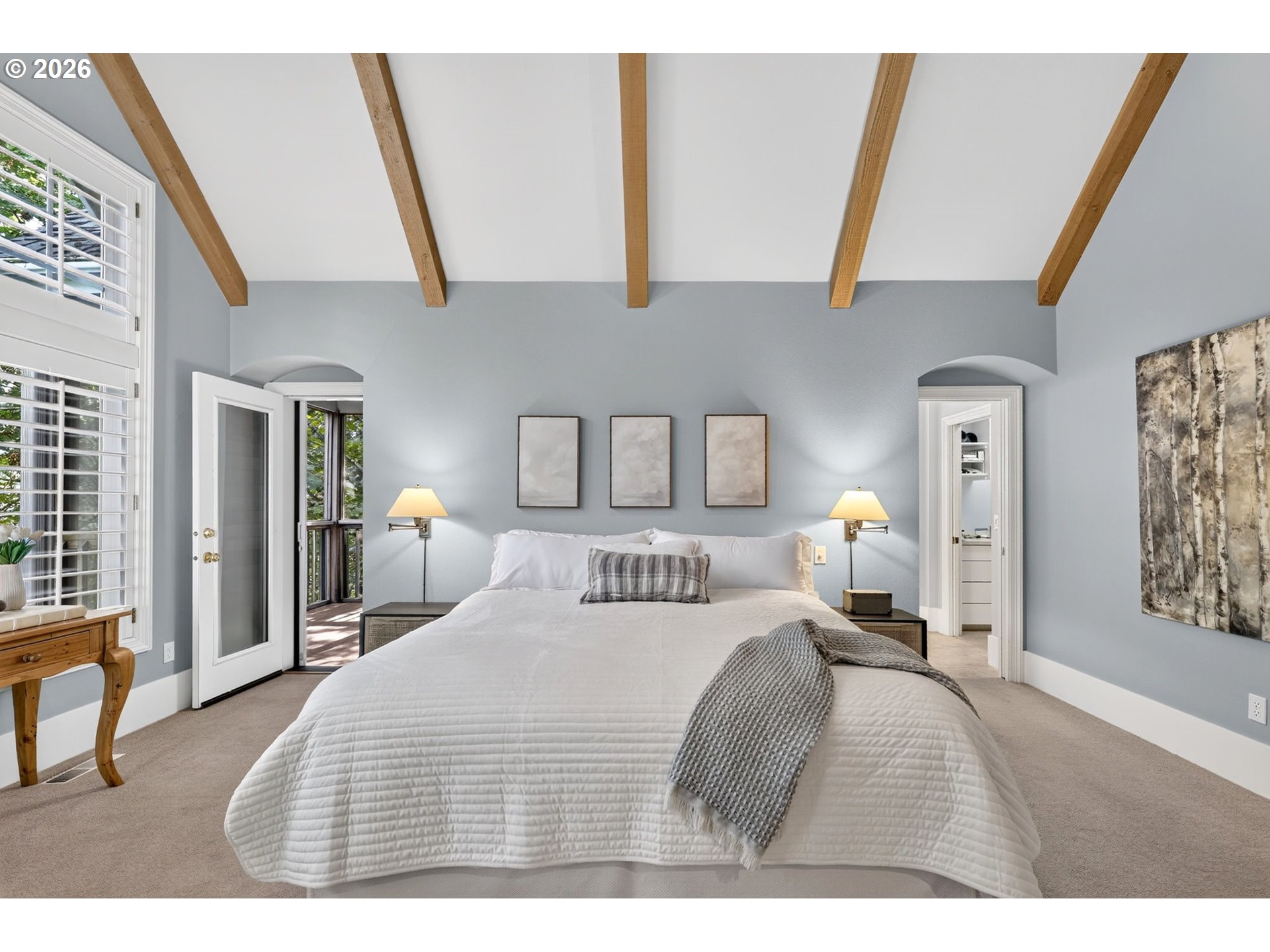 Bedroom with a white bed beneath exposed wood ceiling beams and an open glass door.