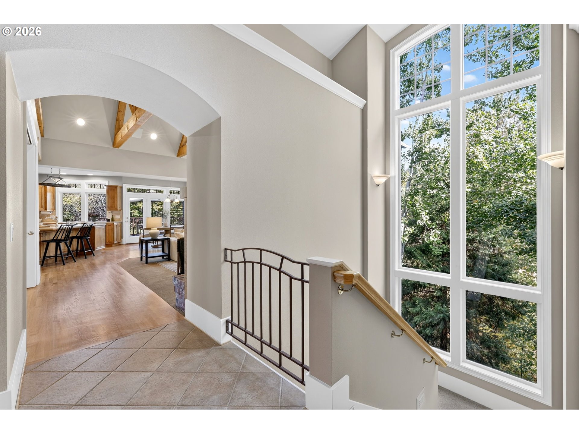 Tiled entry landing beside a tall window, looking through an archway toward the vaulted kitchen and living area.