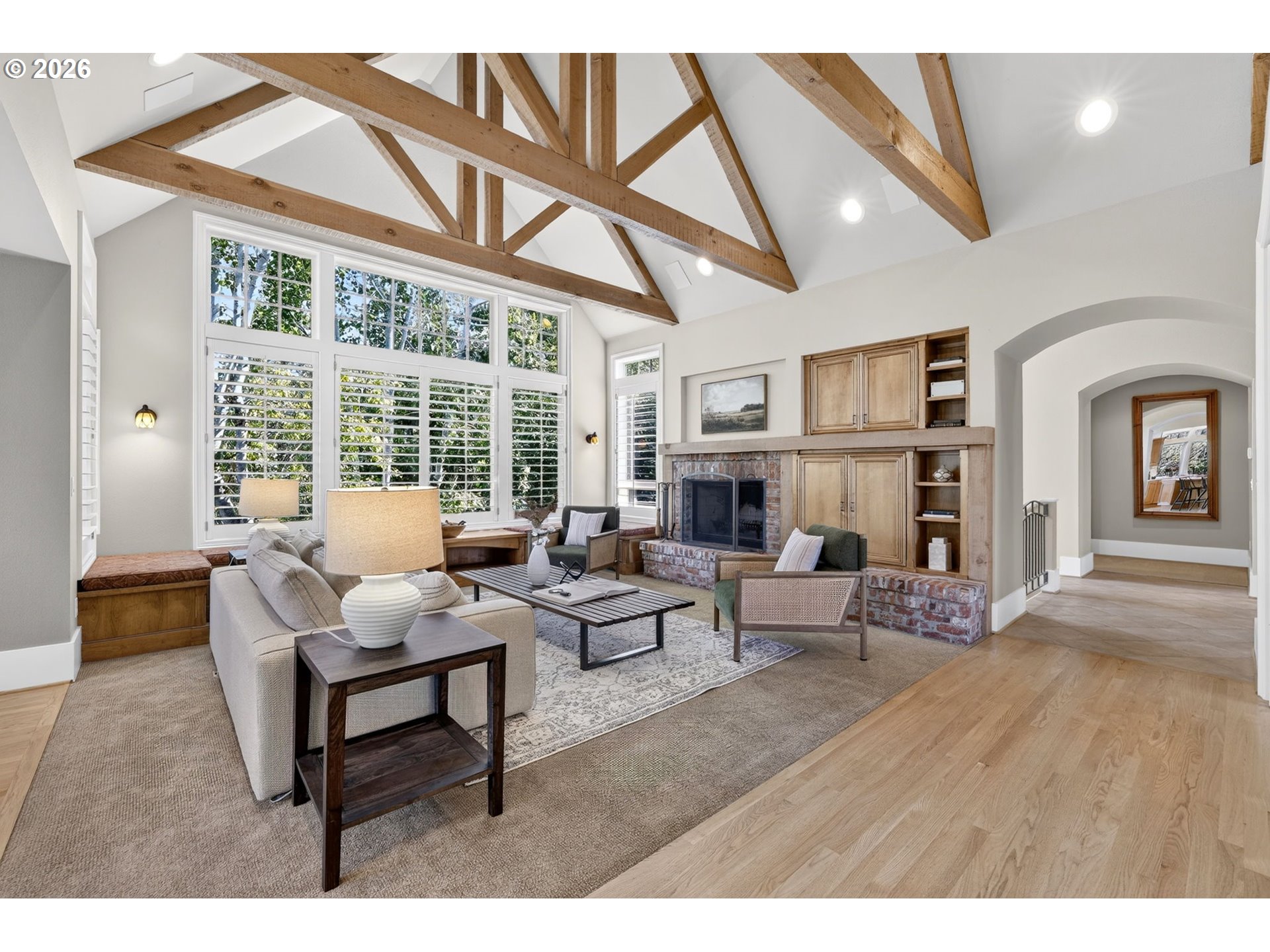 Living room with exposed timber ceiling trusses, large windows, and a brick fireplace.