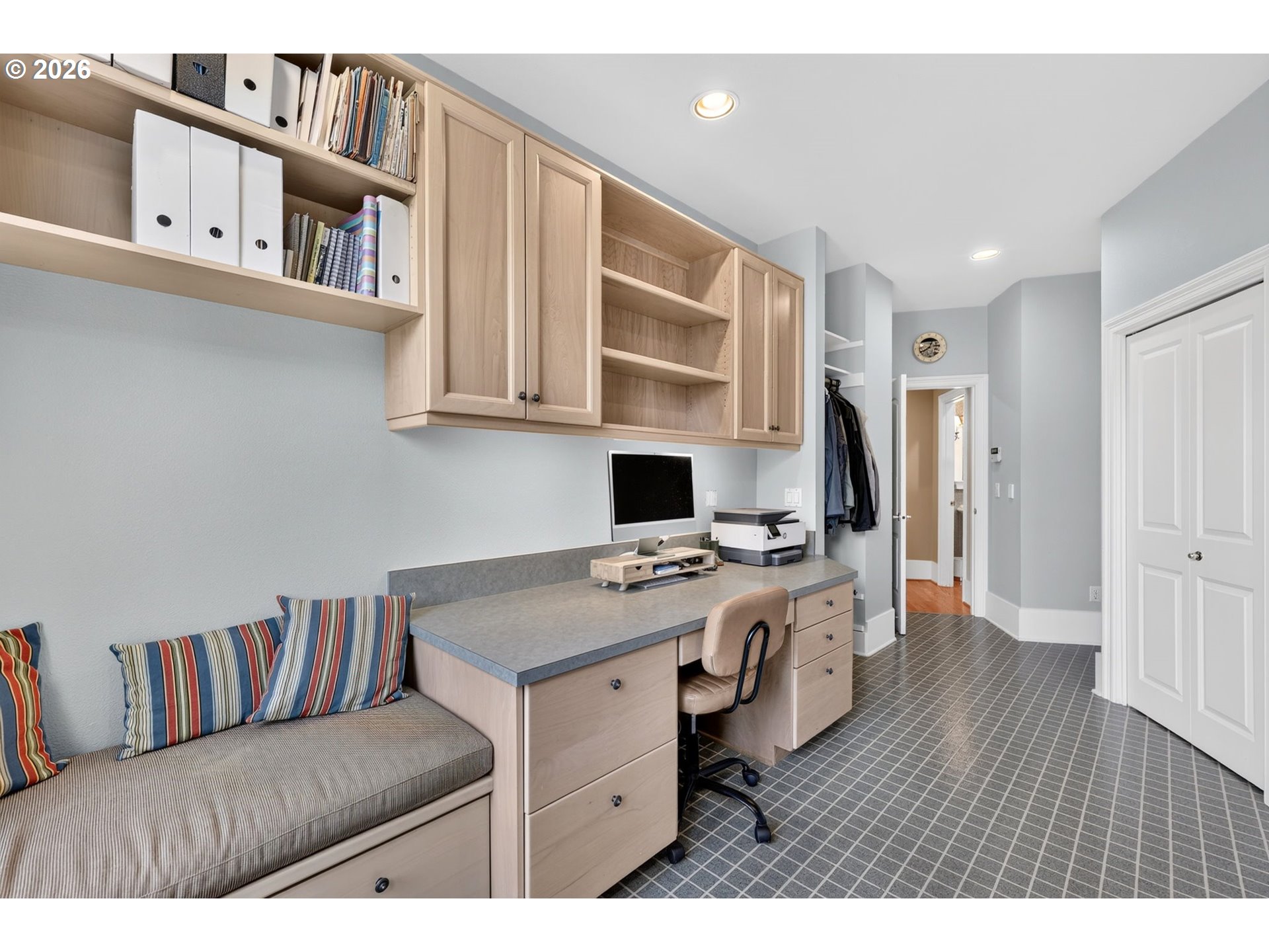 Home office with built-in desk, light wood cabinetry, and a cushioned bench with striped pillows.