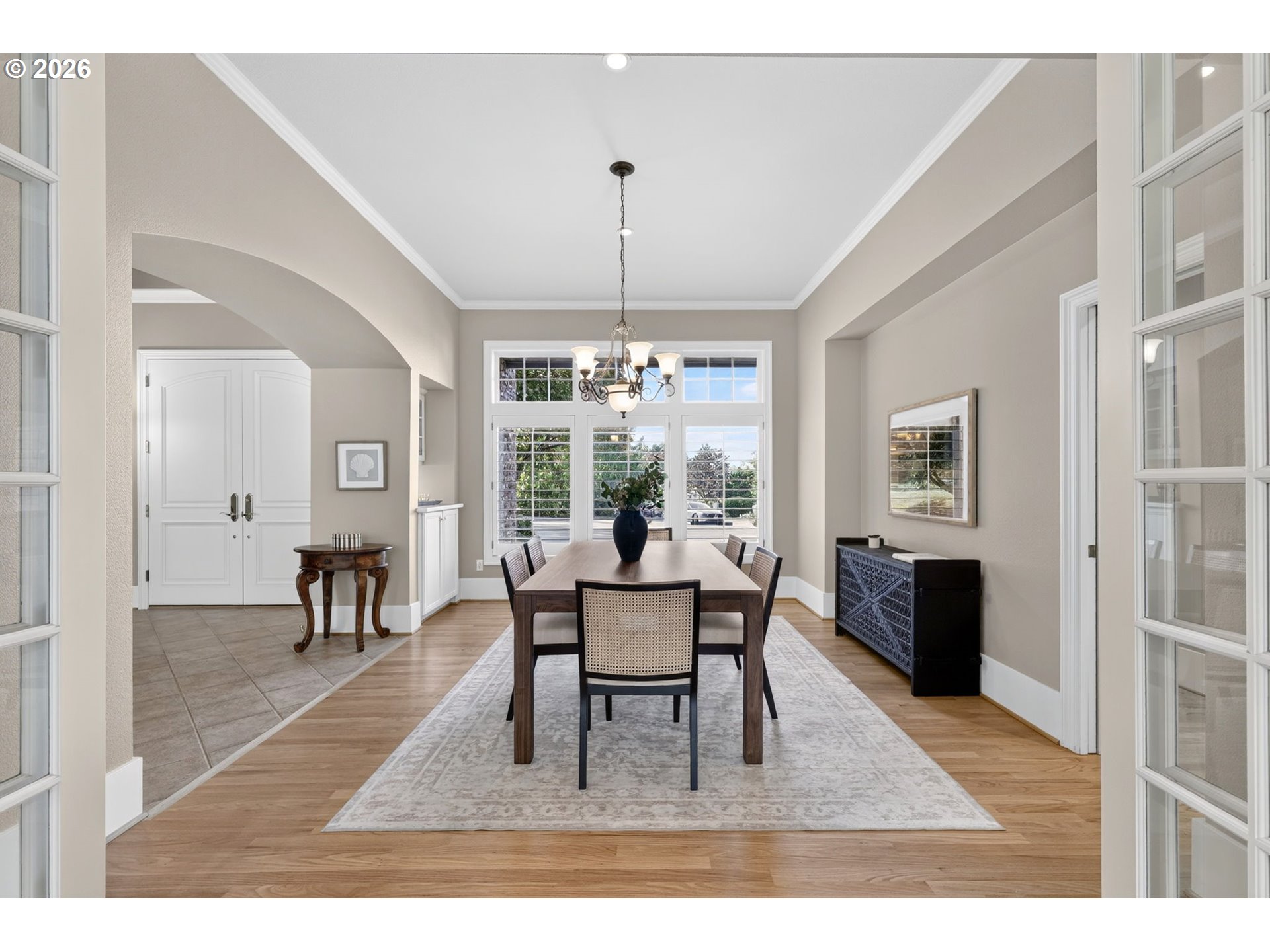Furnished dining room with a wooden table, chandelier, large windows, and hardwood floors.