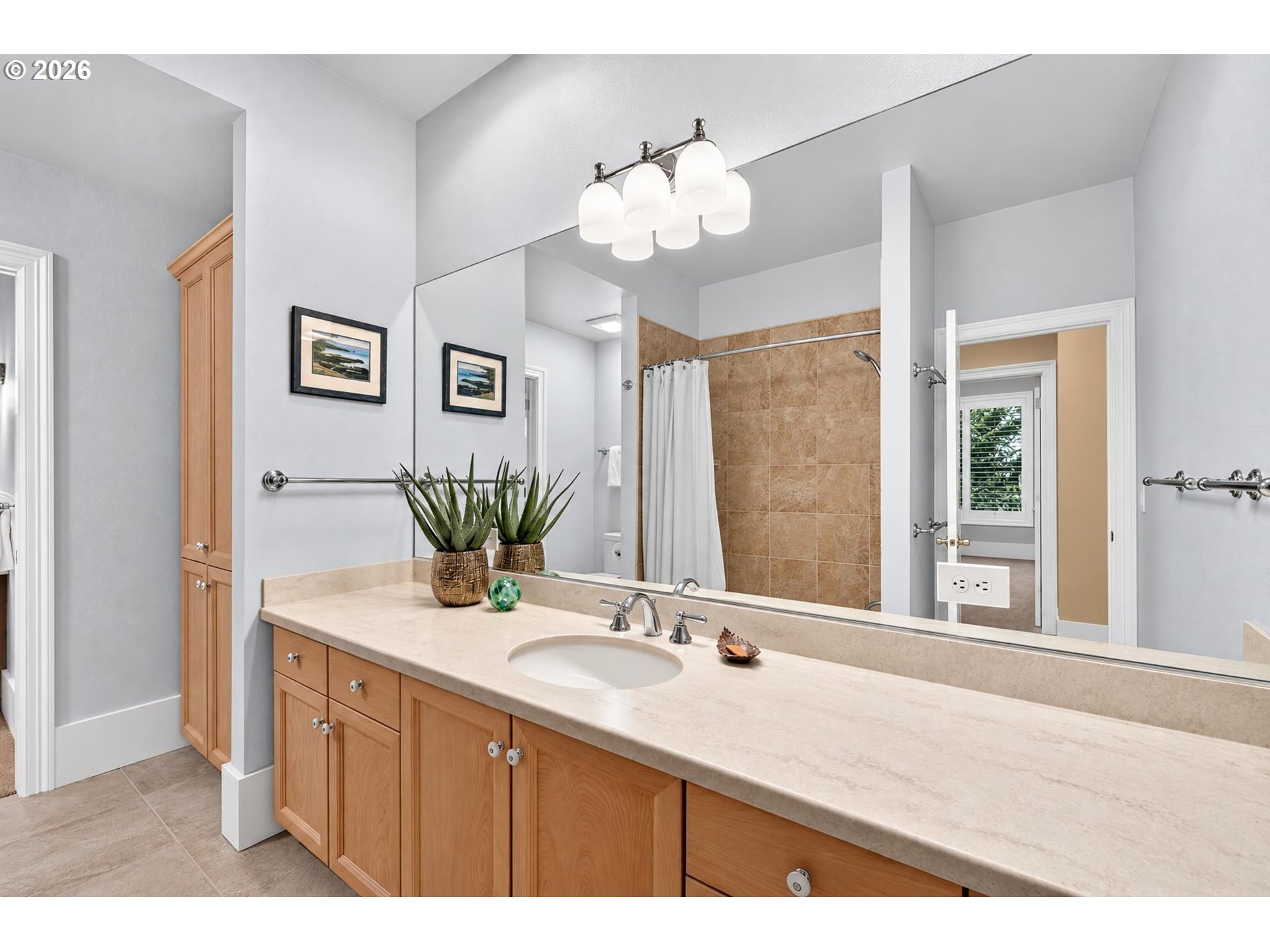 Bathroom with a long wood vanity, beige countertop, large mirror, and tiled shower.