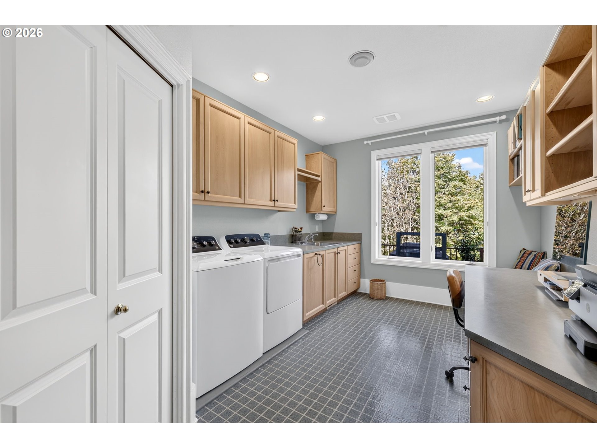 Laundry room with washer and dryer, light wood cabinets, and a long counter beside a large window.