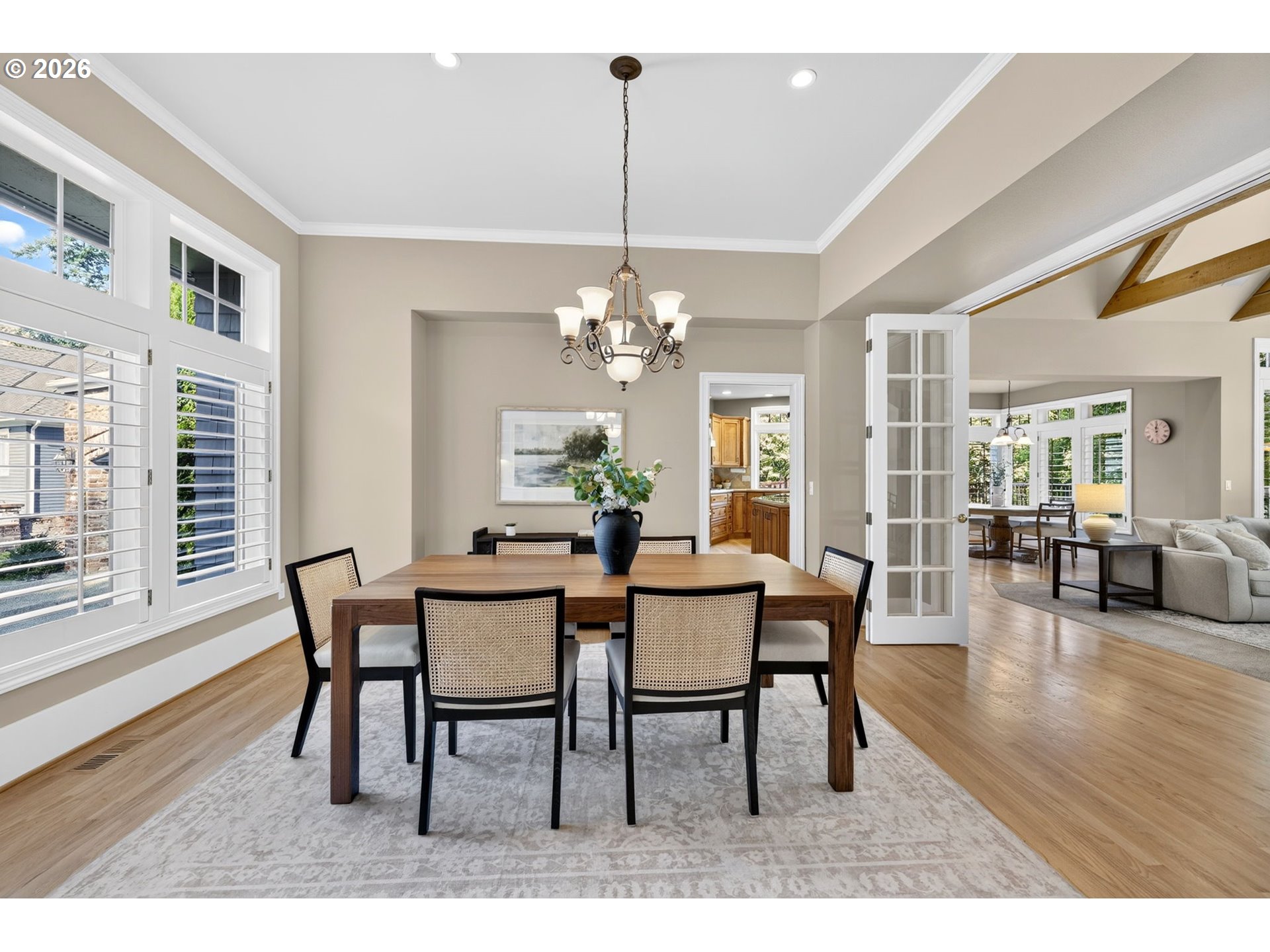 Dining room with a dark wood table, woven chairs, tall shuttered windows, and an open doorway to the living room.