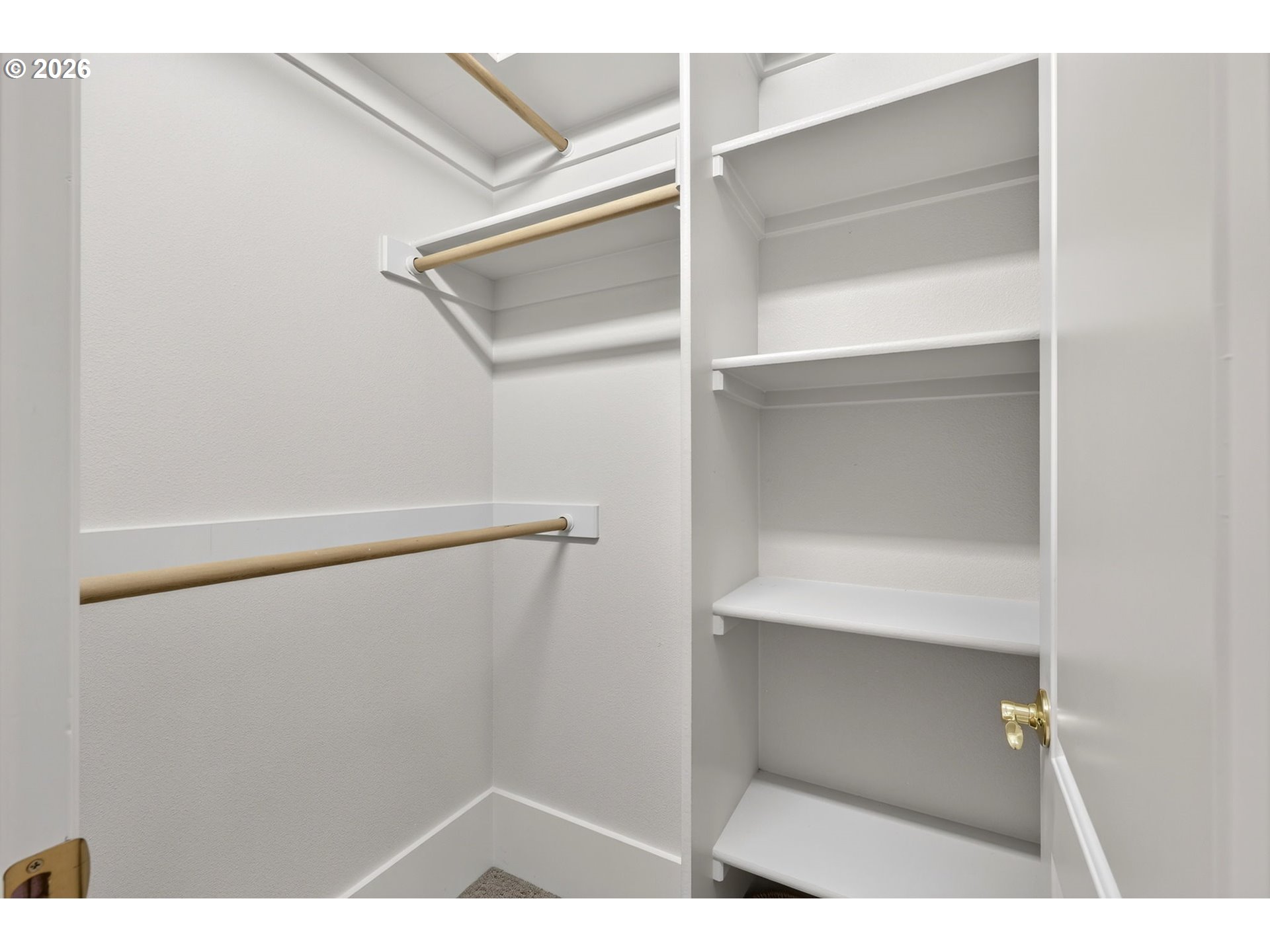 Empty walk-in closet with white built-in shelves and wooden hanging rods.