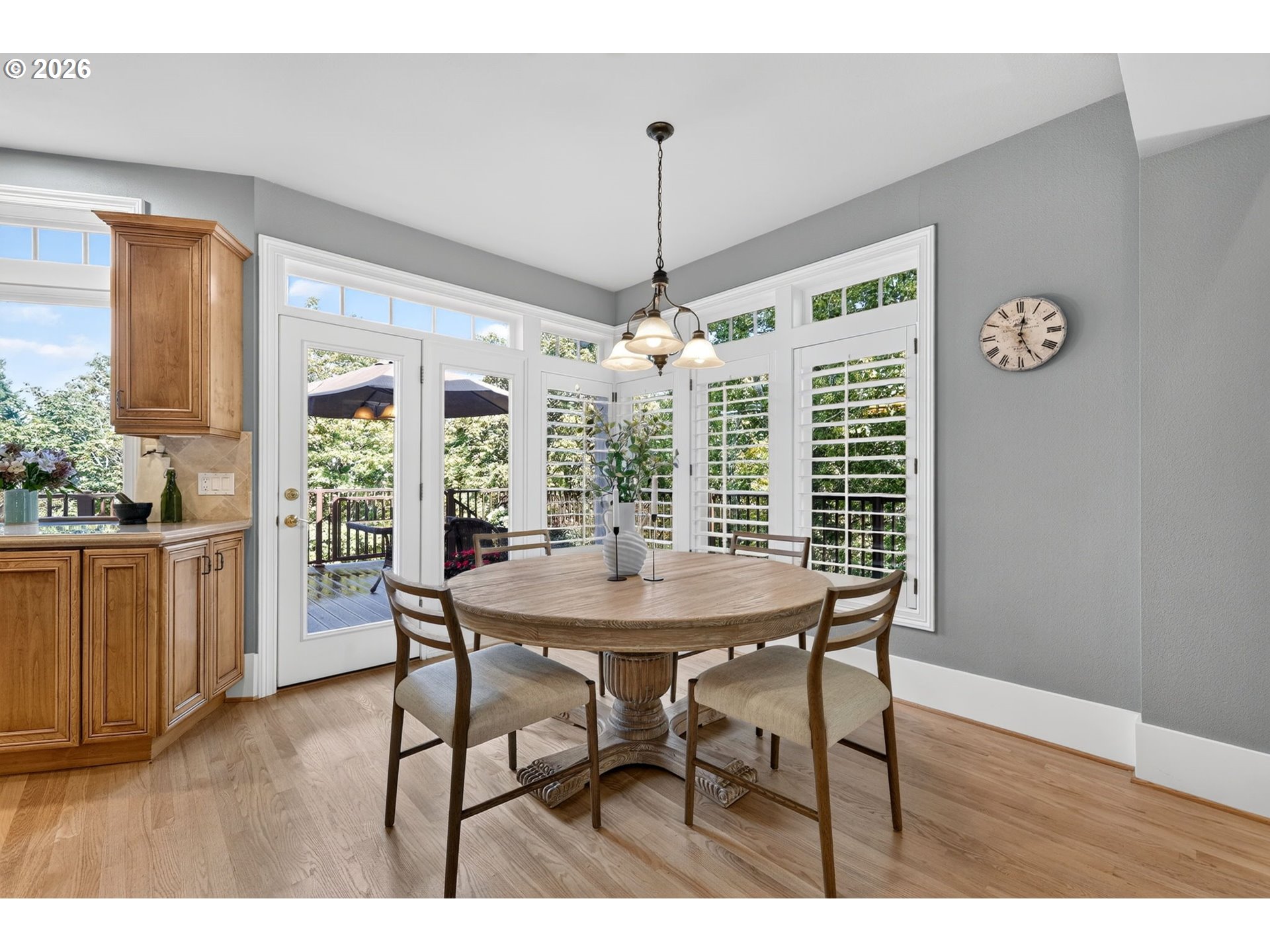 Dining area with a round wood table, white plantation shutters, and glass doors to a deck.