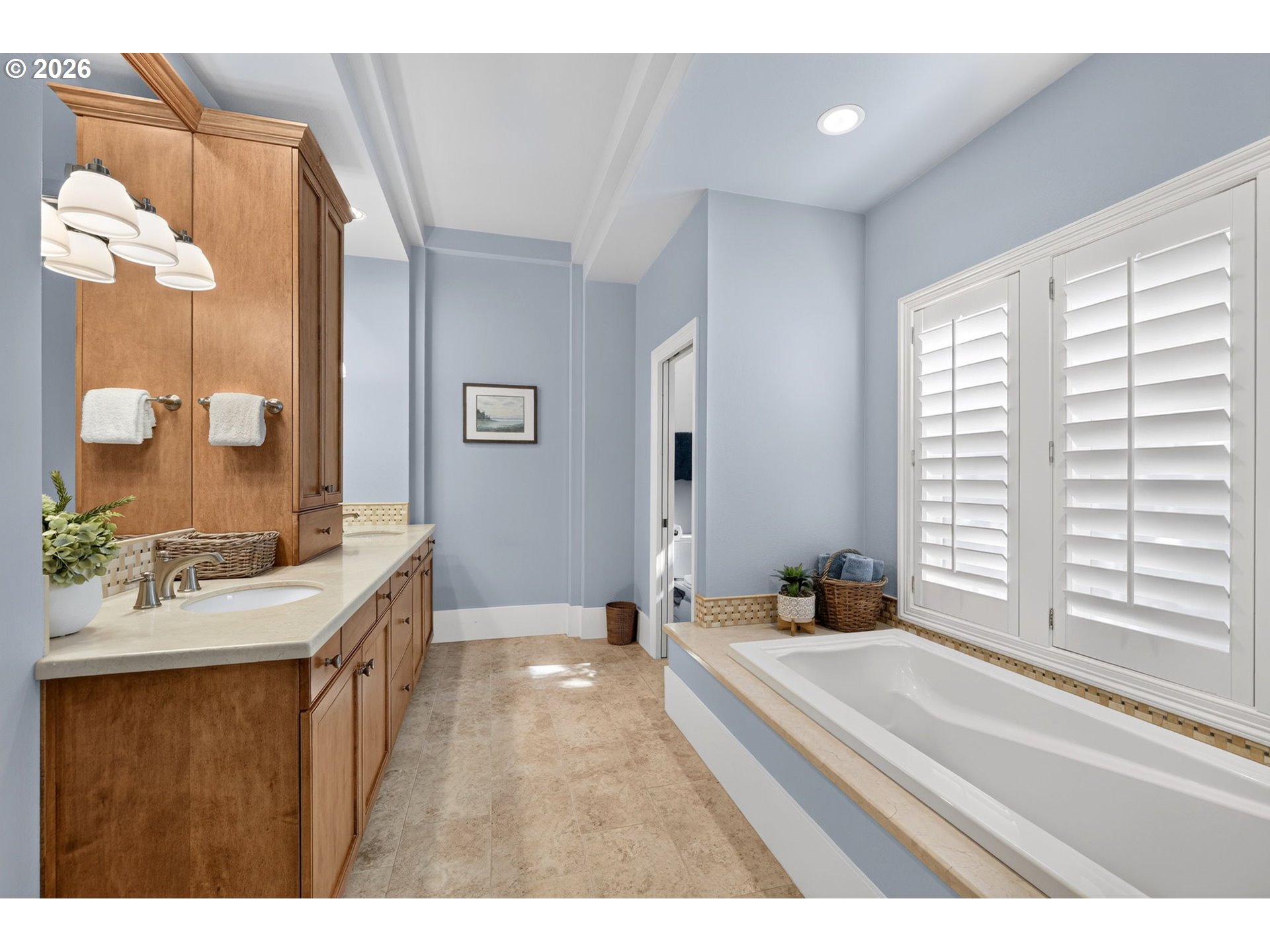 Bathroom with a long bathtub beneath plantation shutters and a wood vanity.