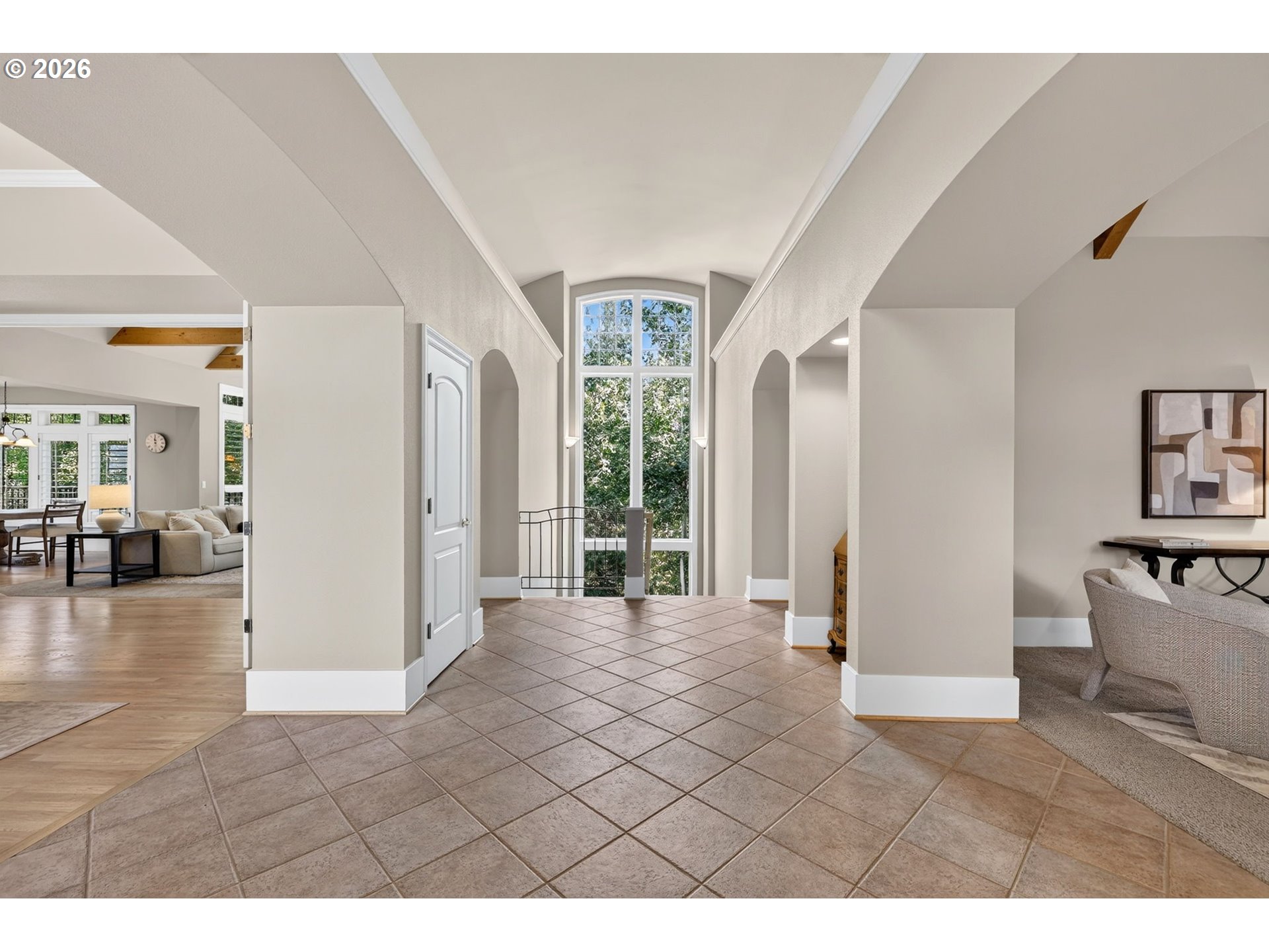 Bright foyer with a tiled floor, arched ceiling, and tall windows overlooking trees.