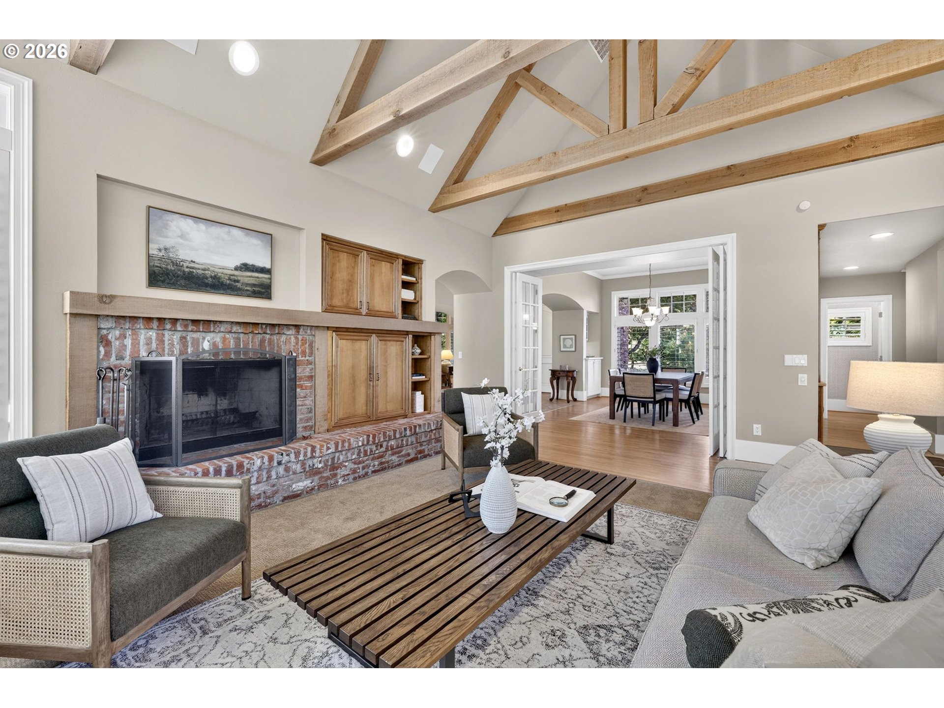 Living room with brick fireplace, built-in cabinetry, and exposed beams on a vaulted ceiling.