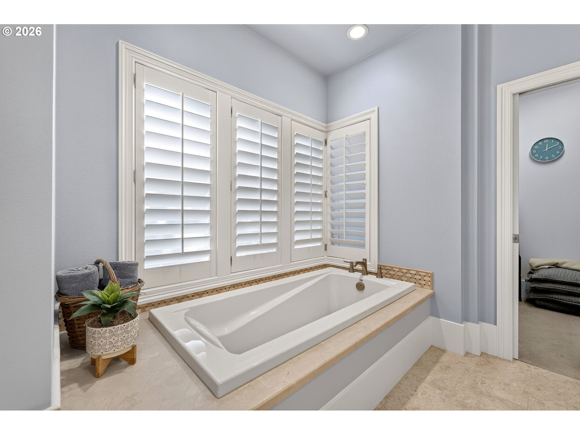 Bathroom with a built-in soaking tub beneath white plantation shutters and a plant beside it.